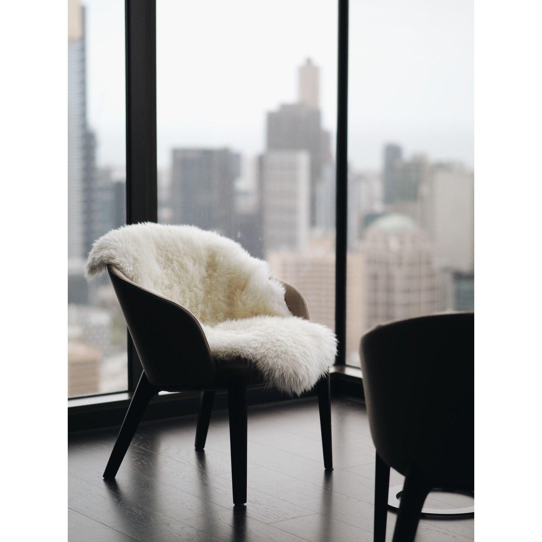 Modern chair with white sheepskin rug draped, set by large window with city skyline view
