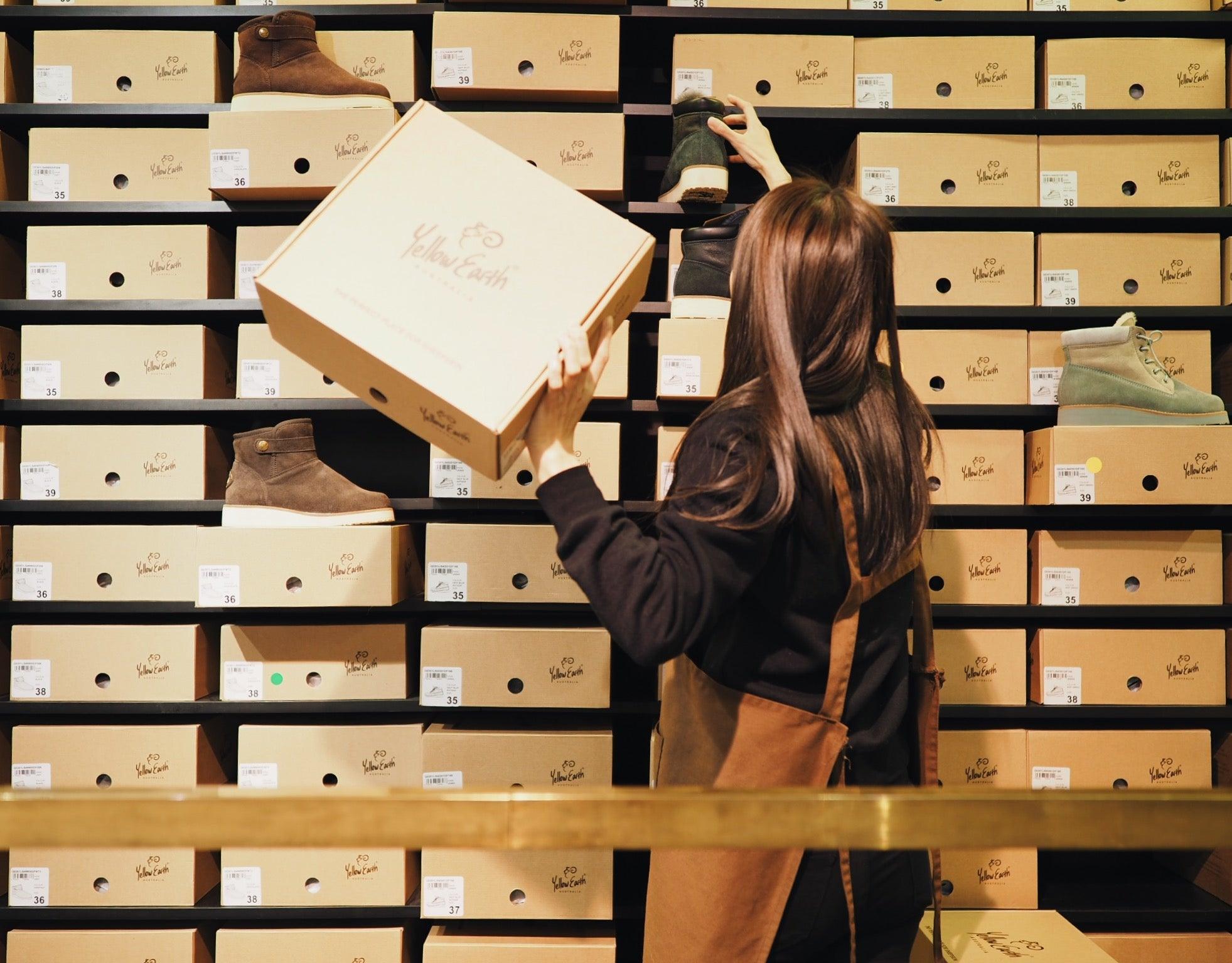 Store worker organizing sheepskin boot boxes on shelves, featuring various UGG boots.