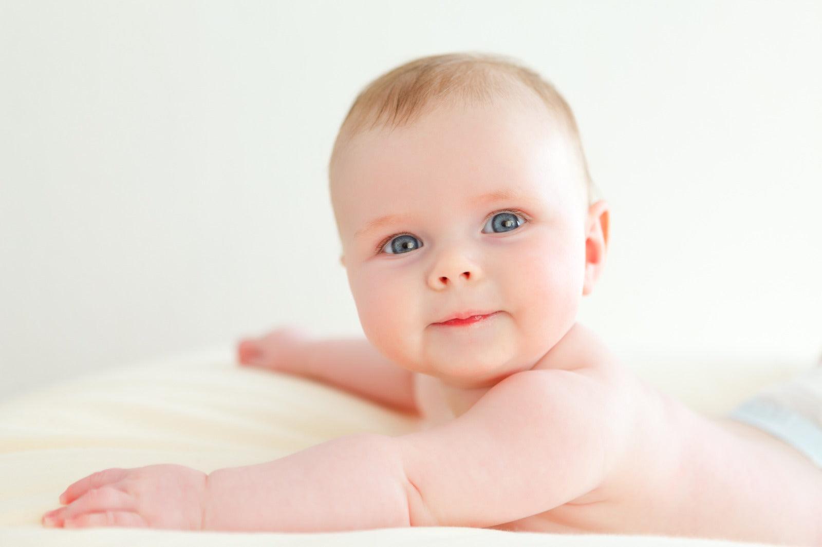 Smiling baby lying on a soft cream sheepskin rug with a light background