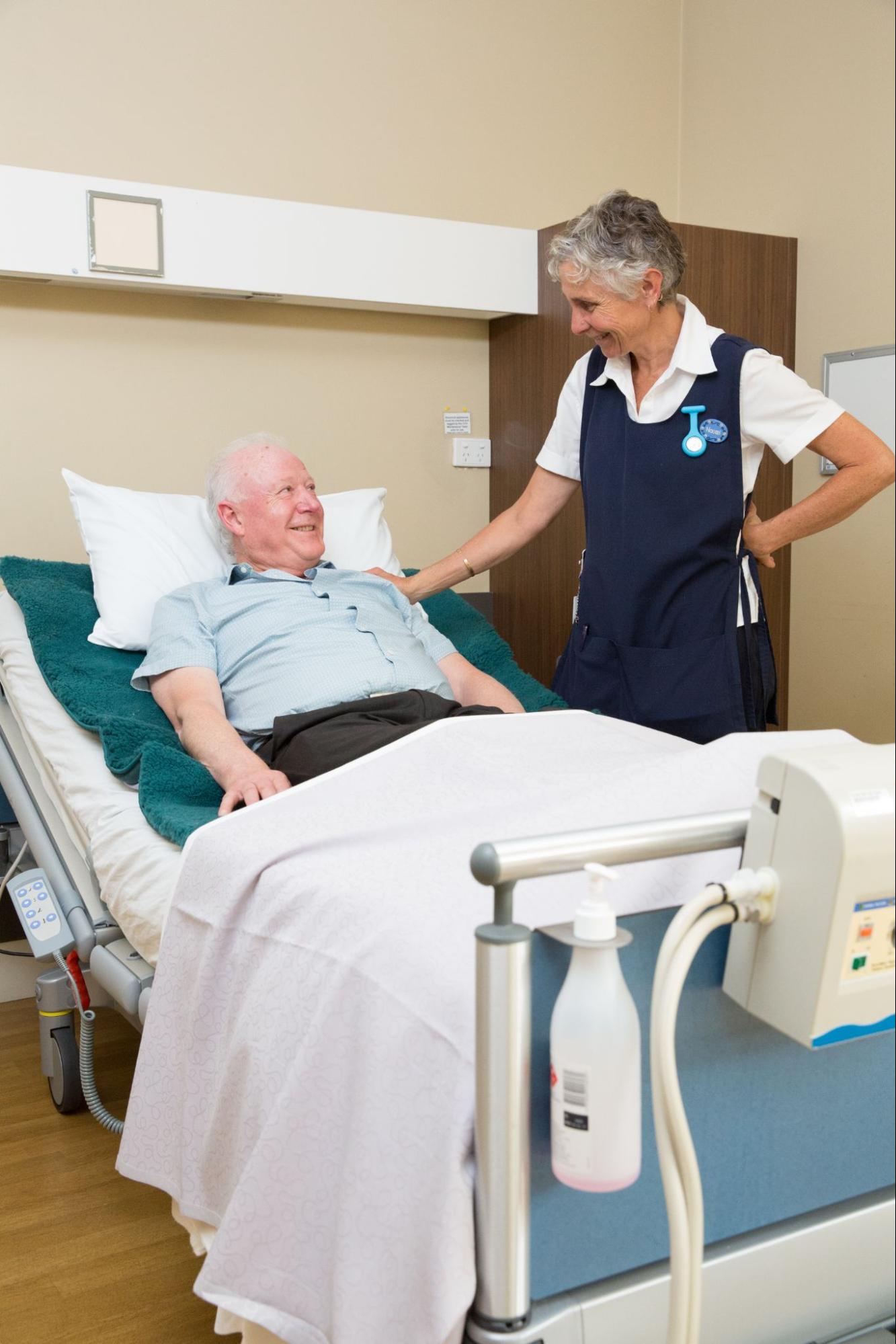 Elderly patient resting on medical sheepskin mattress in hospital bed with nurse attending.
