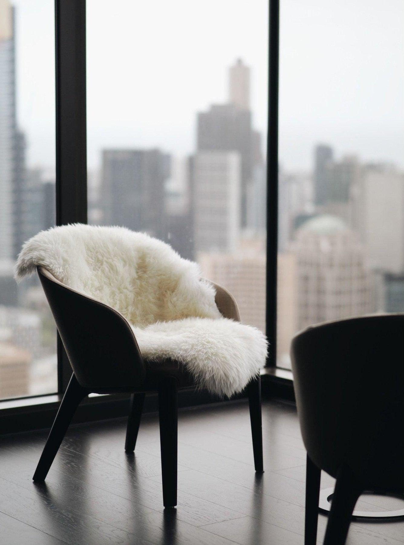 White sheepskin rug draped over modern chair in high-rise apartment with city view