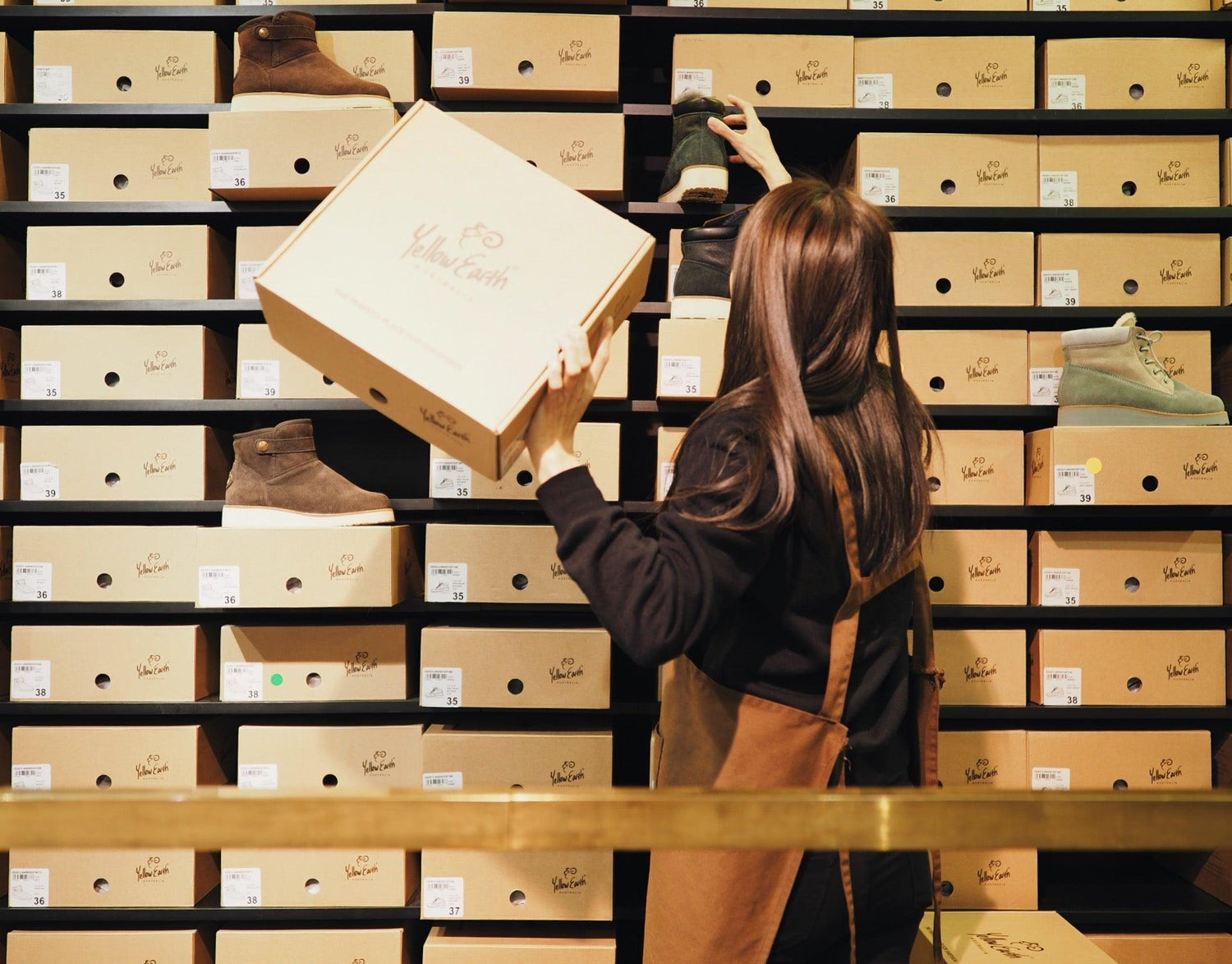 Store worker organizing sheepskin boot boxes on shelves, featuring various UGG boots.