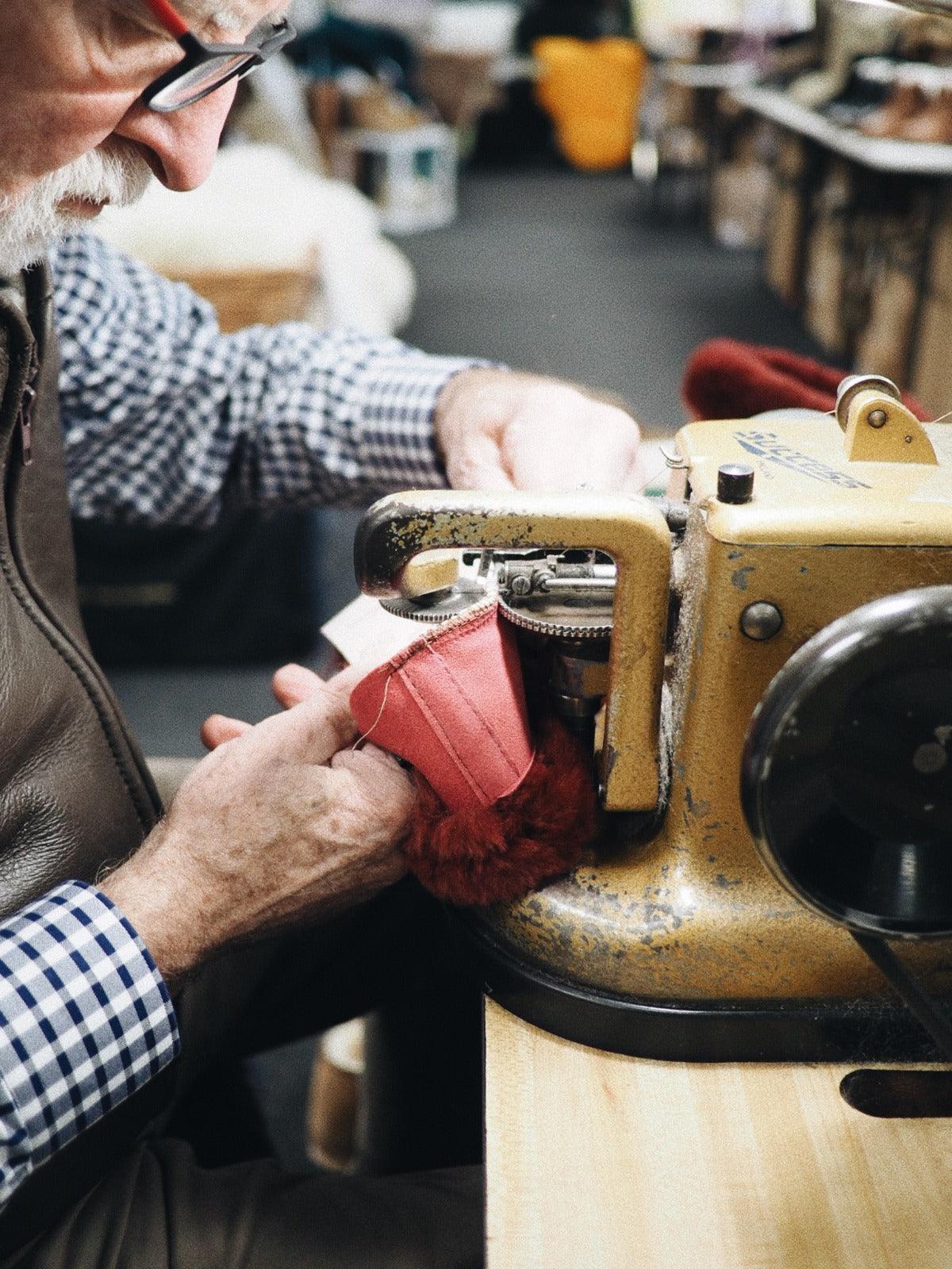 Artisan sewing pink sheepskin boot with heavy duty machine in workshop