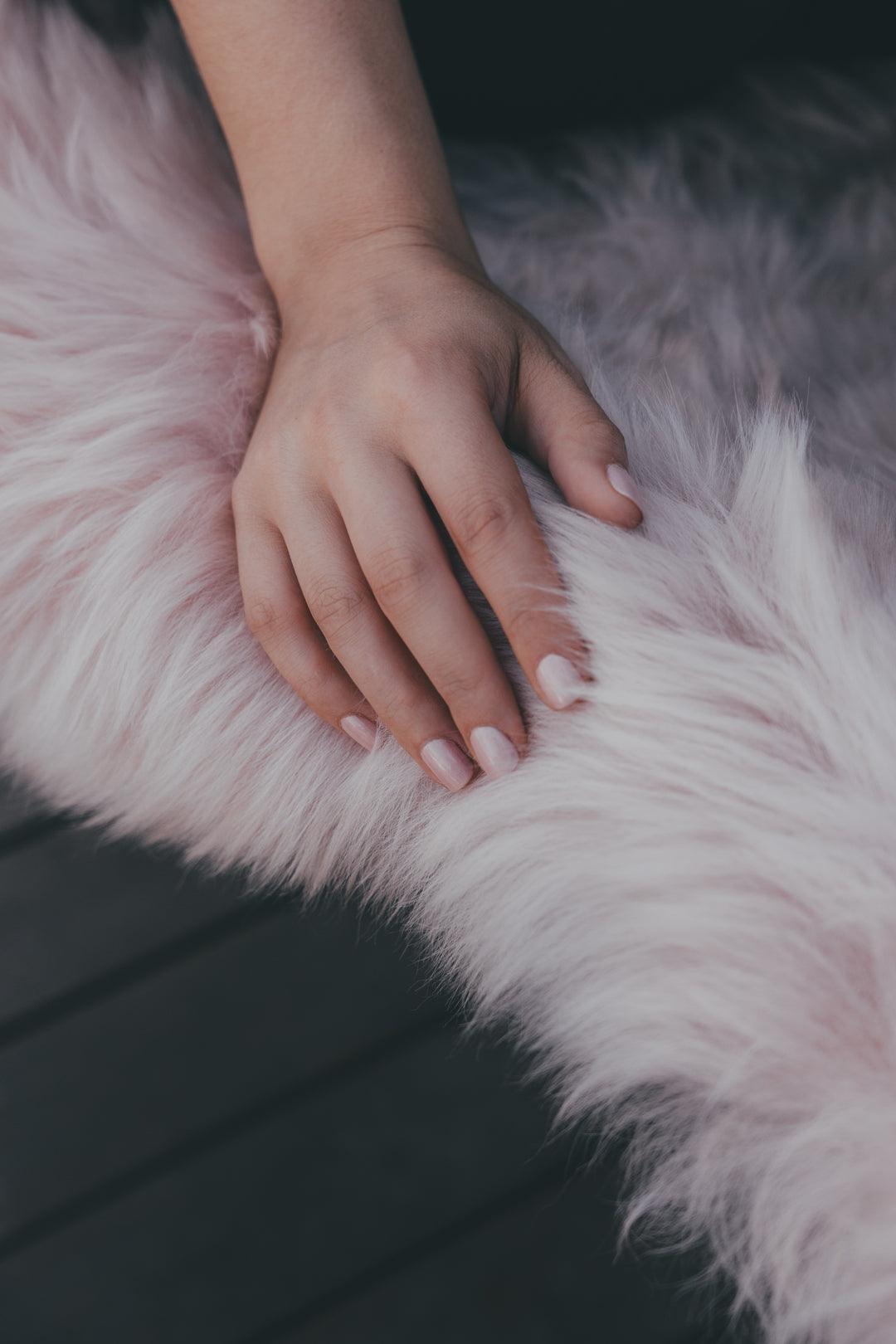 Hand touching soft pink sheepskin rug, showcasing premium sheepskin texture