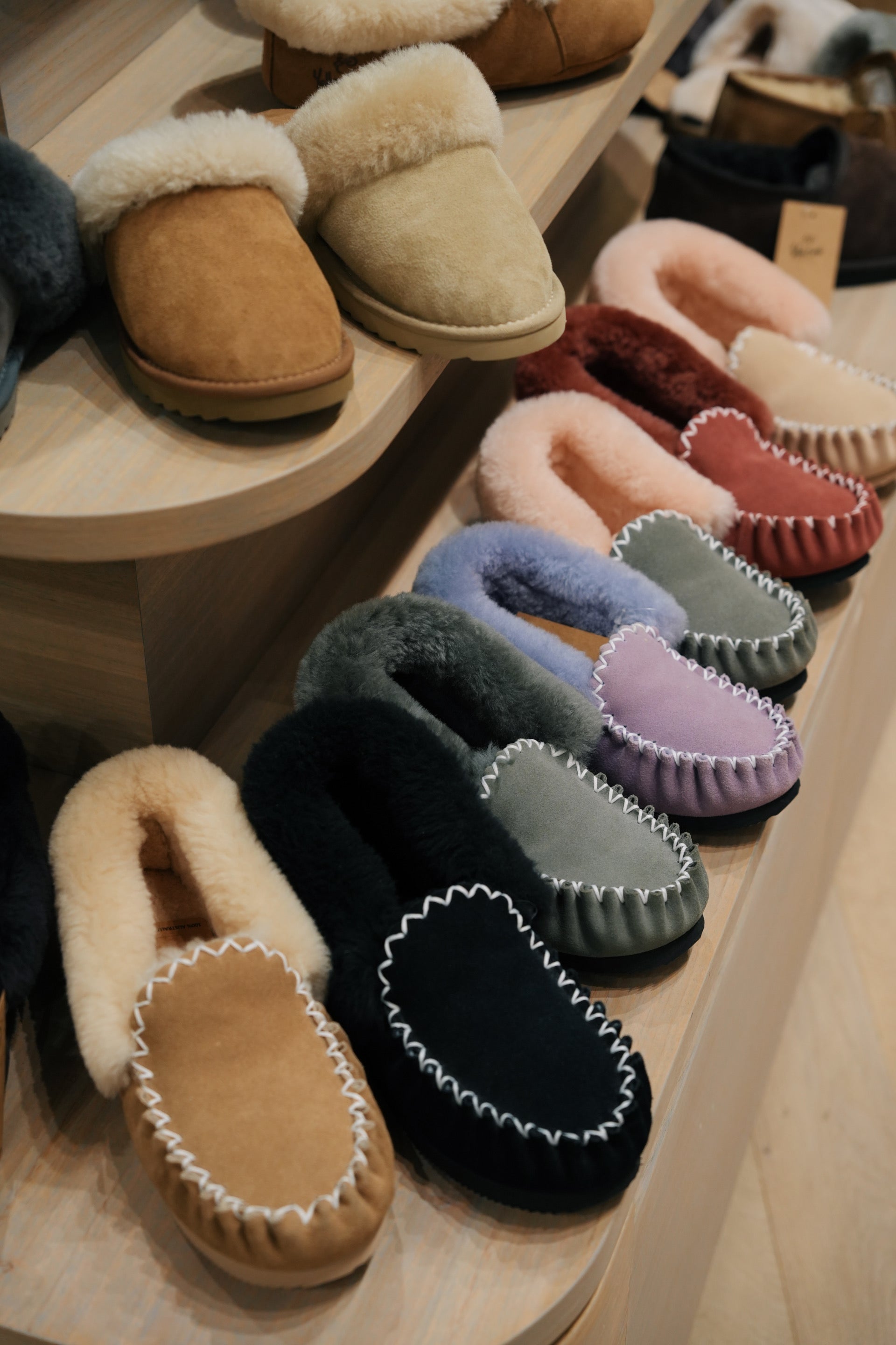 Assorted sheepskin moccasin slippers in various colors displayed on wooden shelves