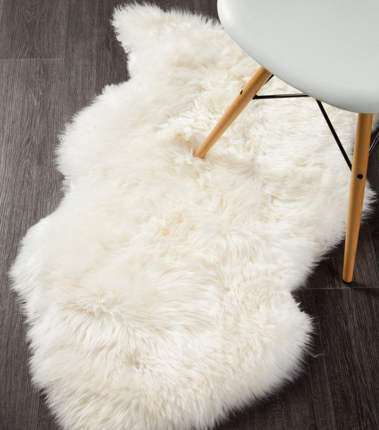 Ivory sheepskin rug on dark wood floor beside modern chair, textured and plush decor accent.