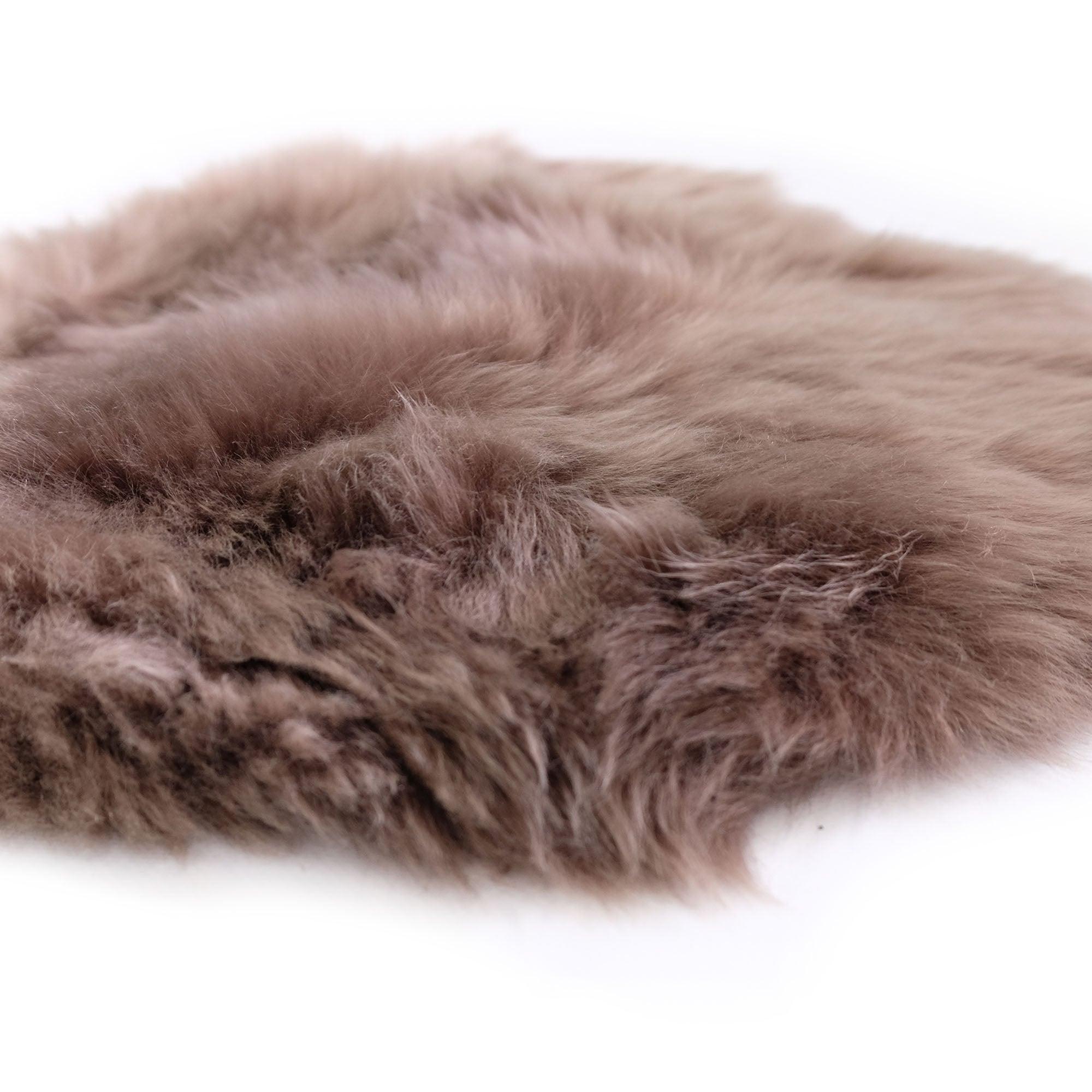 Close-up of round taupe sheepskin rug with soft, fluffy texture on white background