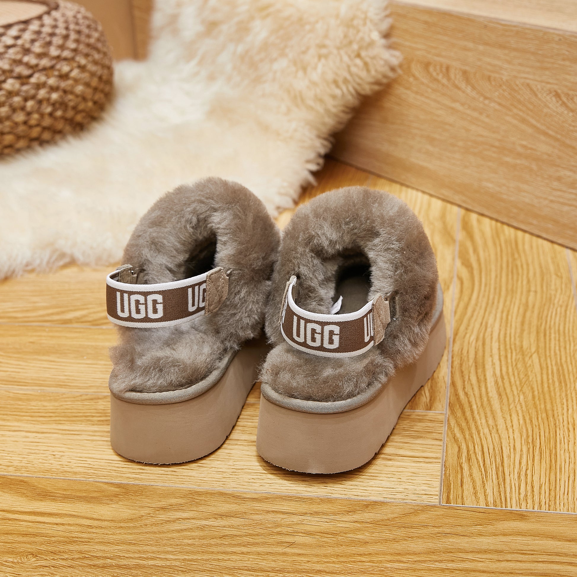 Pair of taupe sheepskin UGG platform slippers with logo strap on wooden floor
