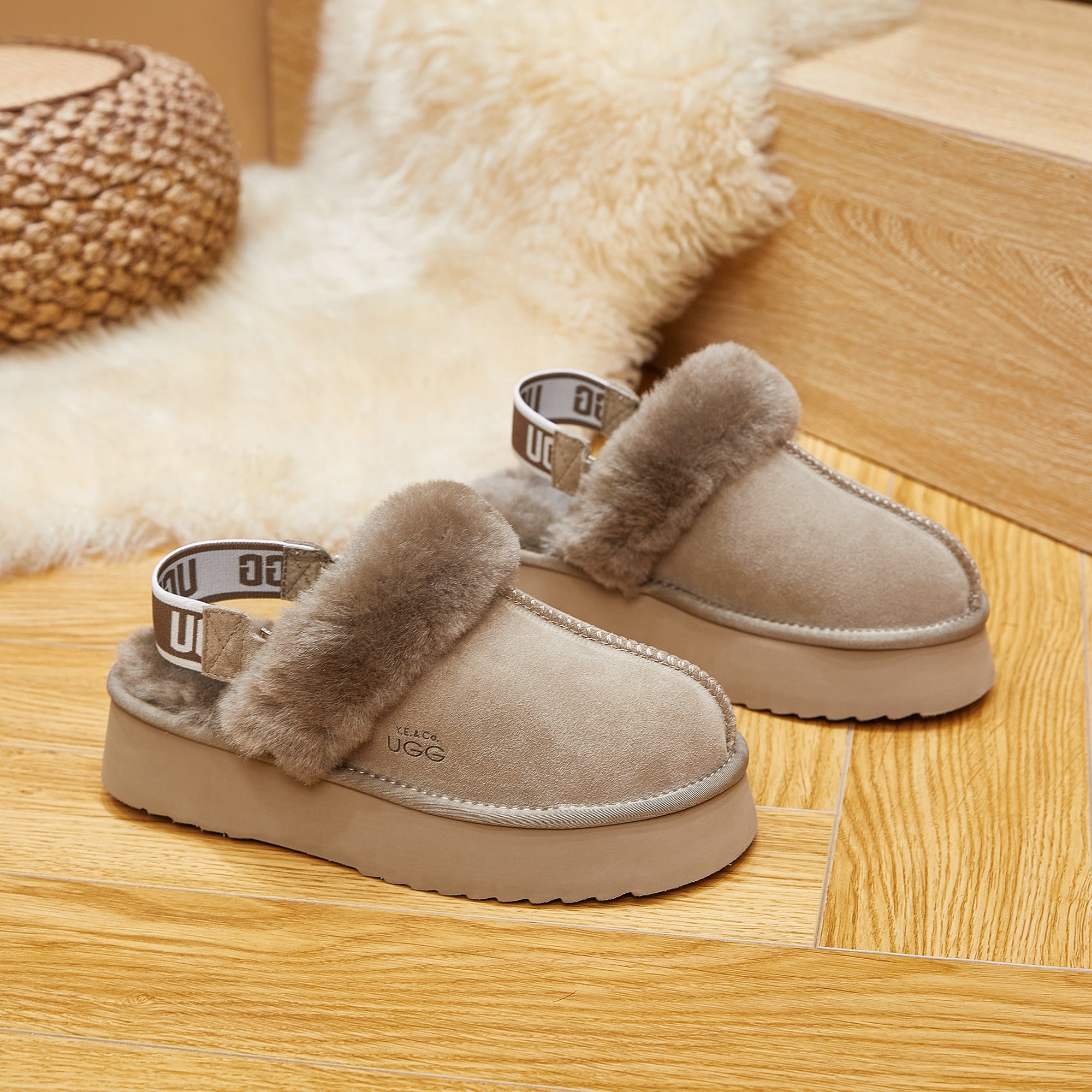 Beige sheepskin UGG slippers with fluffy lining and branded strap on wooden floor
