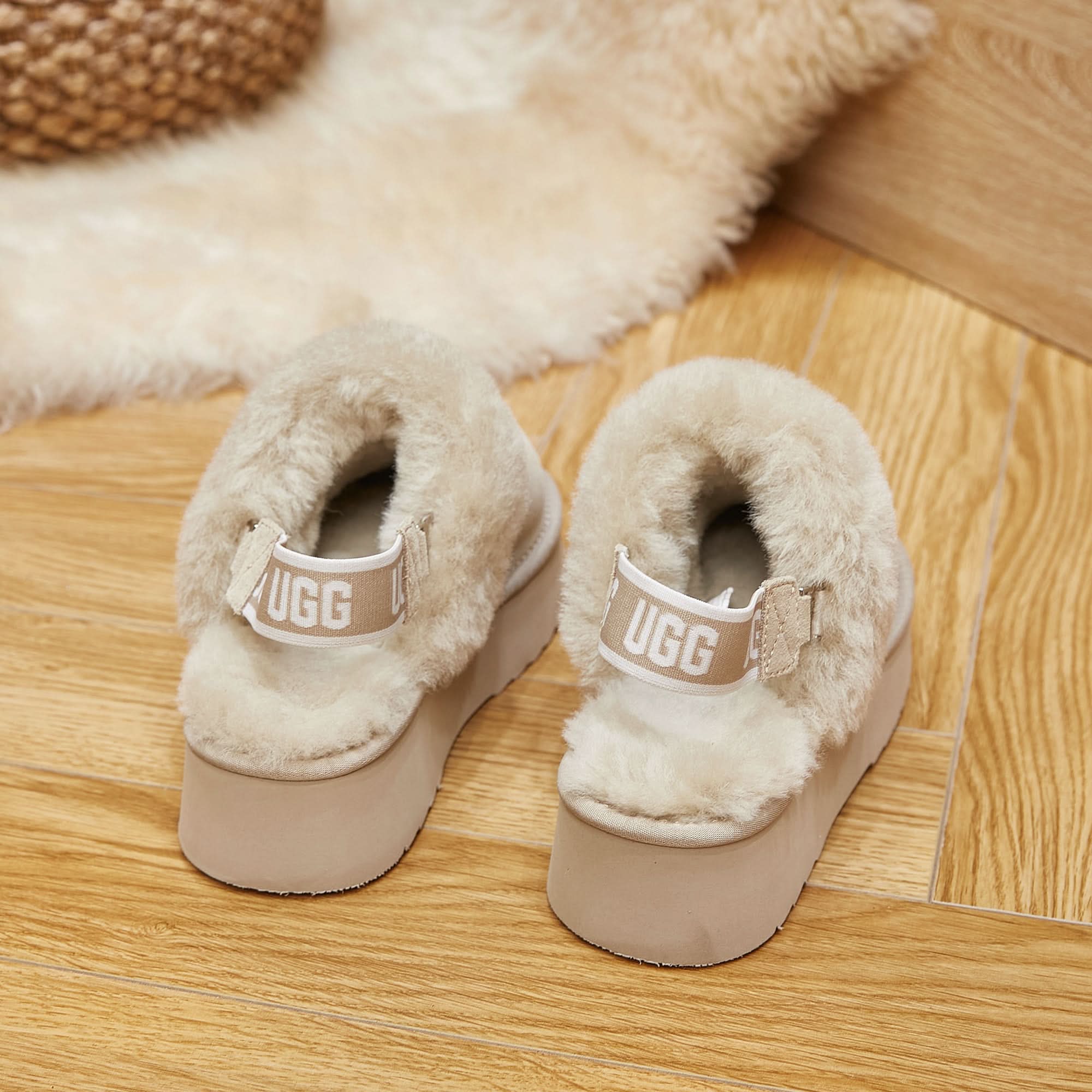 Beige sheepskin UGG platform slippers on wooden floor with matching sheepskin rug