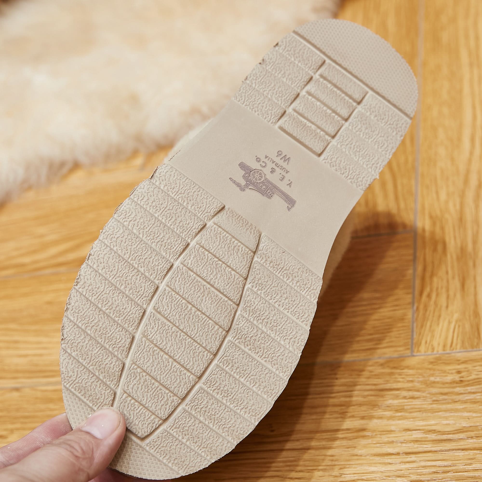 Close-up of textured rubber sole of a sheepskin boot on wooden floor with rug