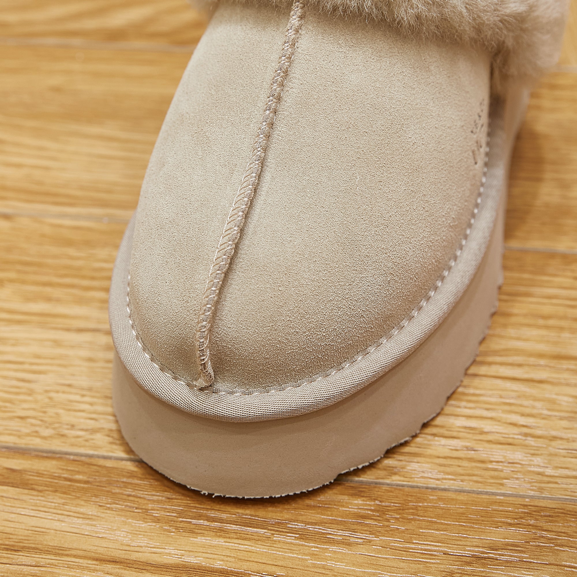 Close-up of beige sheepskin UGG boot with thick sole on wooden floor