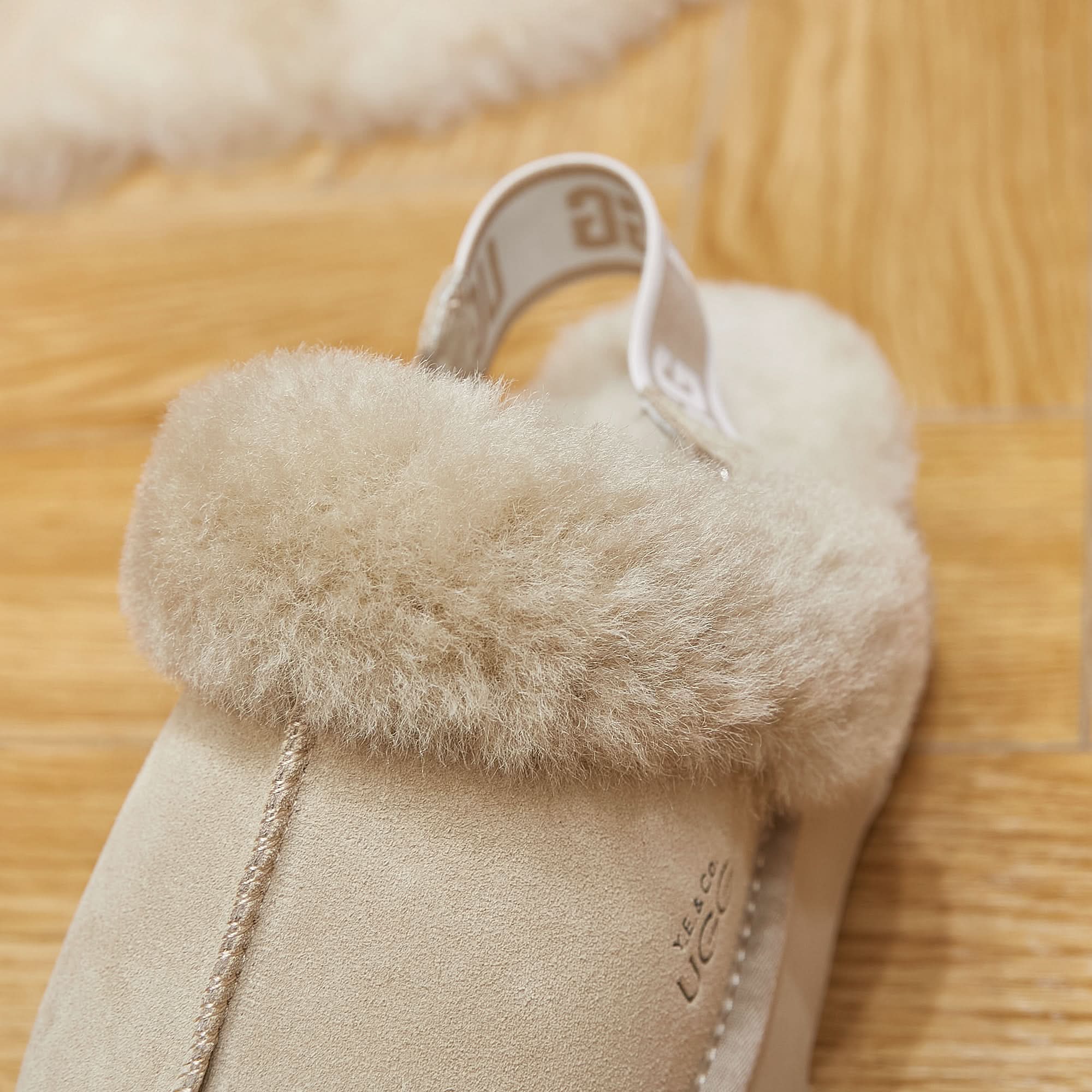 Beige sheepskin UGG slipper with fluffy wool collar on wooden floor
