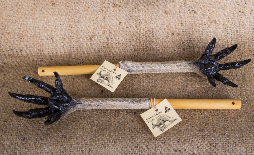 Two black kangaroo paw back scratchers with wooden handles on beige wool texture. - Yellow Earth Australia