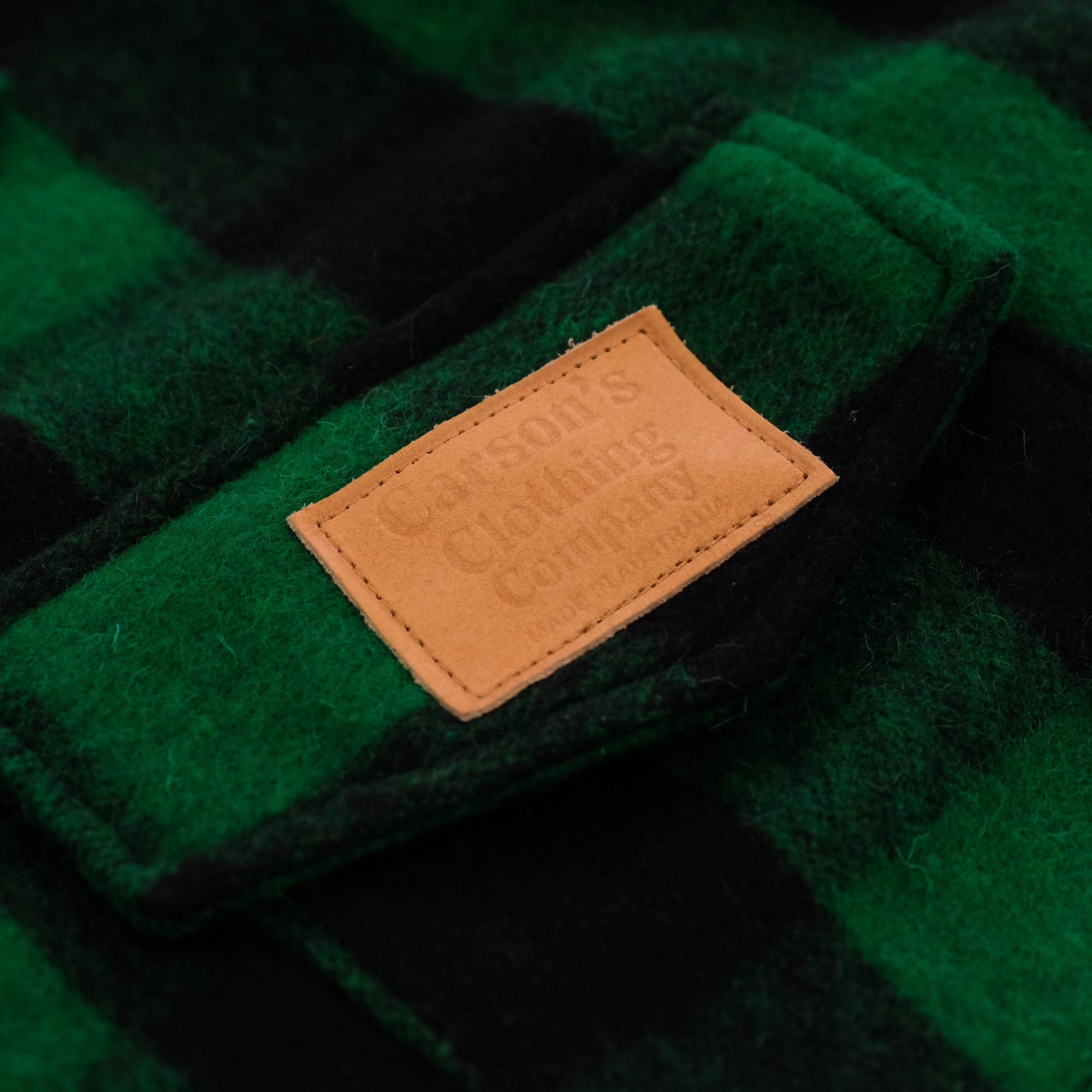 Tan leather care label on green wool fabric close-up detail view. - Yellow Earth Australia