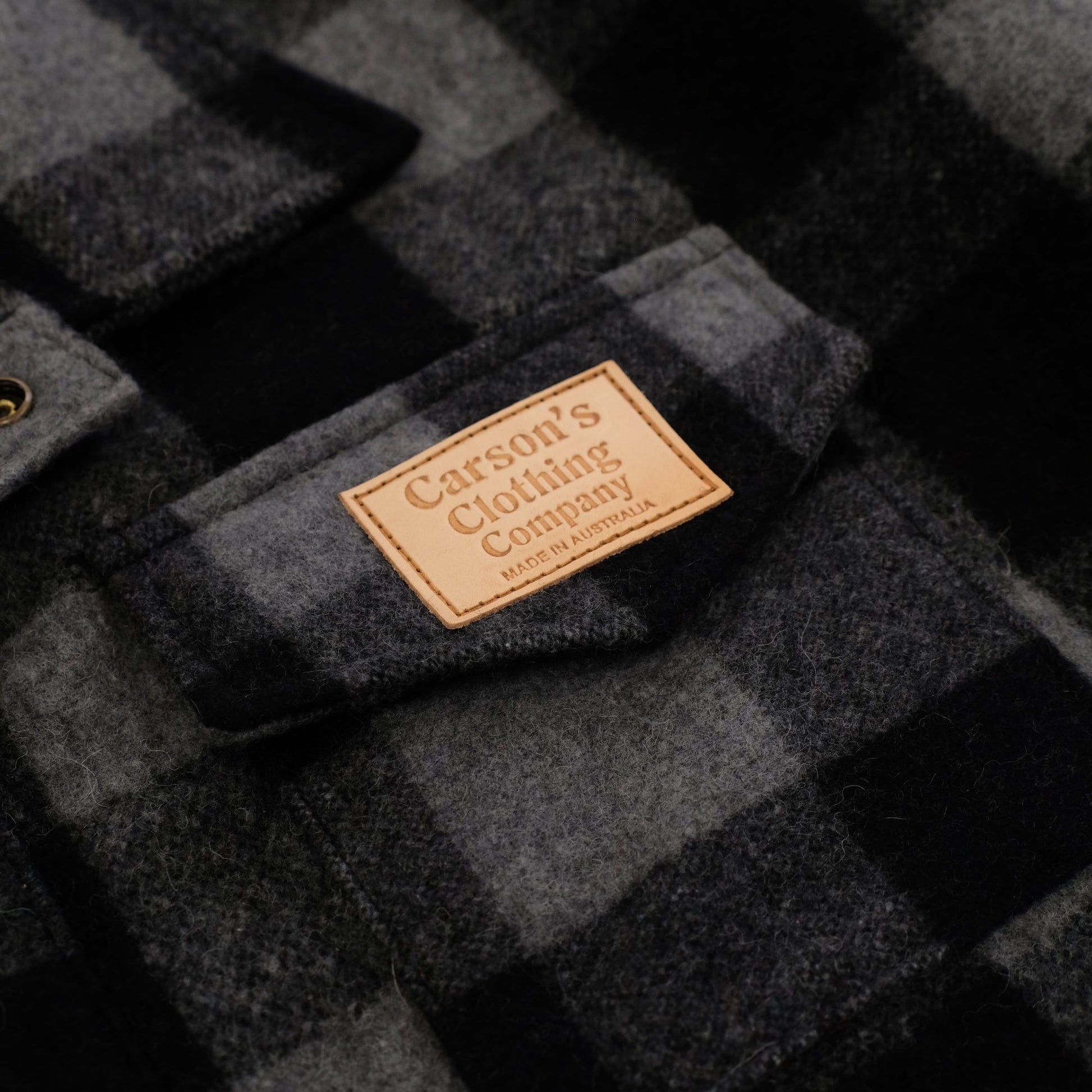 Charcoal wool jacket with quilted texture and tan leather brand label, flat lay view. - Yellow Earth Australia