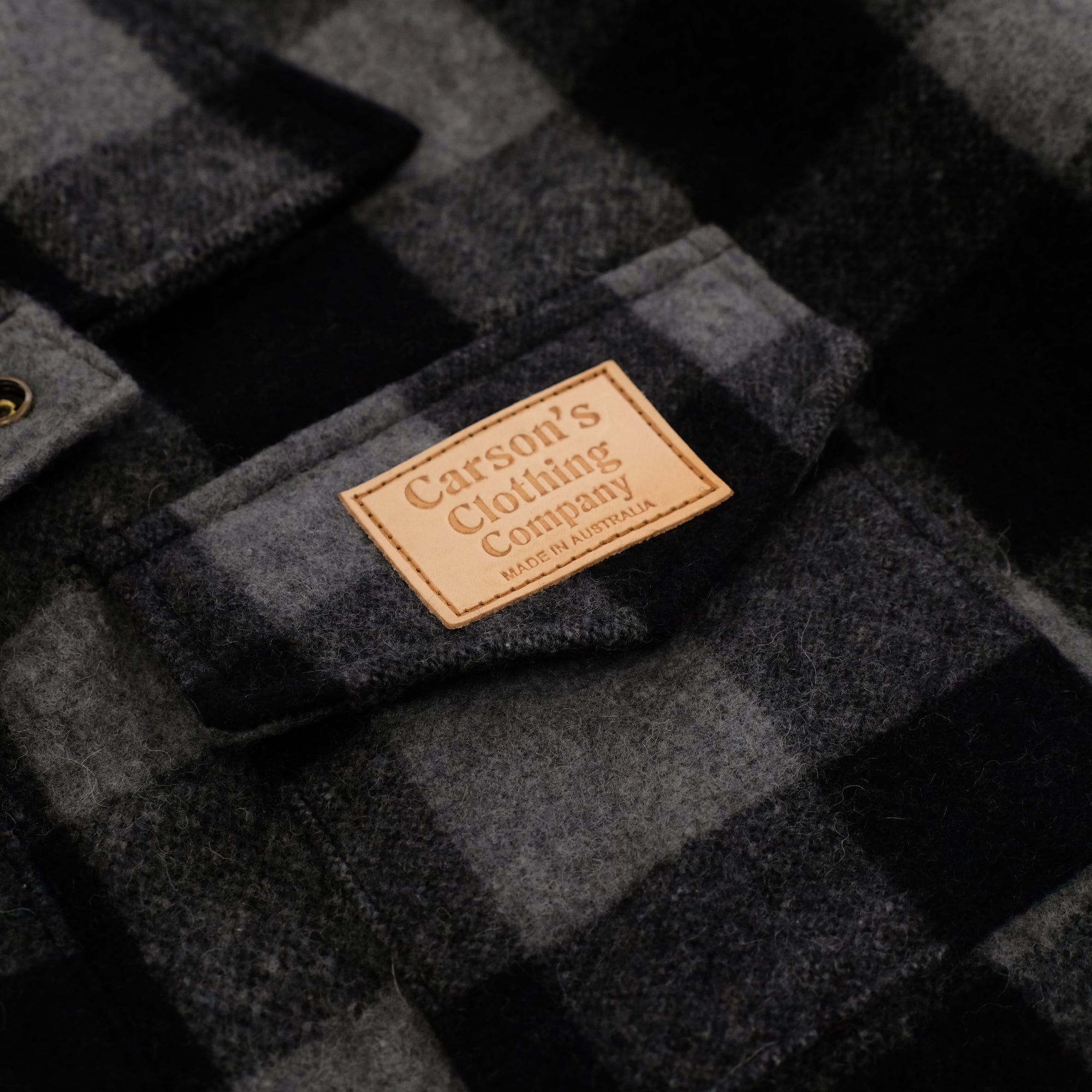 Charcoal wool jacket with quilted texture and tan leather brand label, flat lay view. - Yellow Earth Australia
