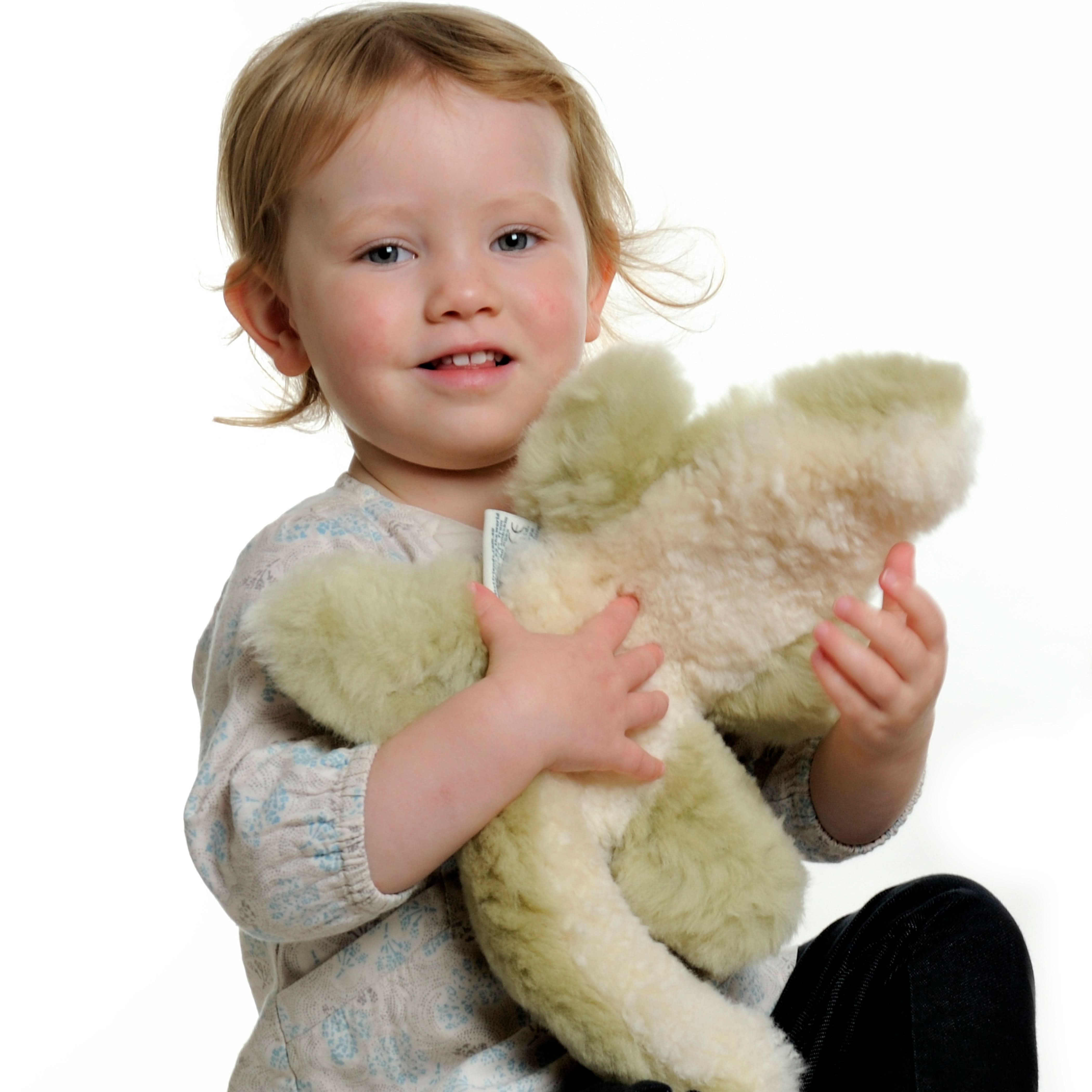 Cream sheepskin teddy bear held by smiling toddler, front view. - Yellow Earth Australia