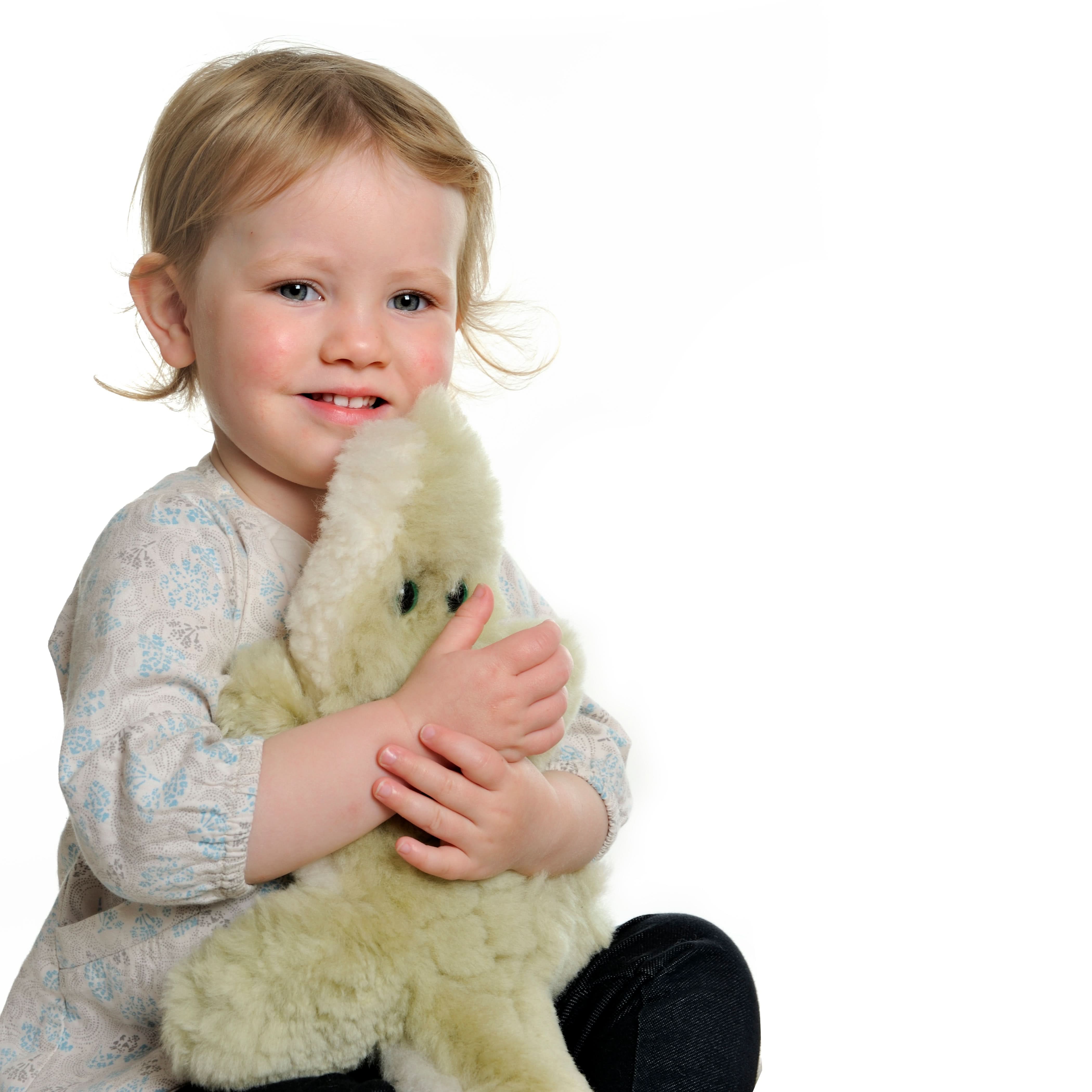 Cream sheepskin toy lamb held by smiling toddler, side view. - Yellow Earth Australia