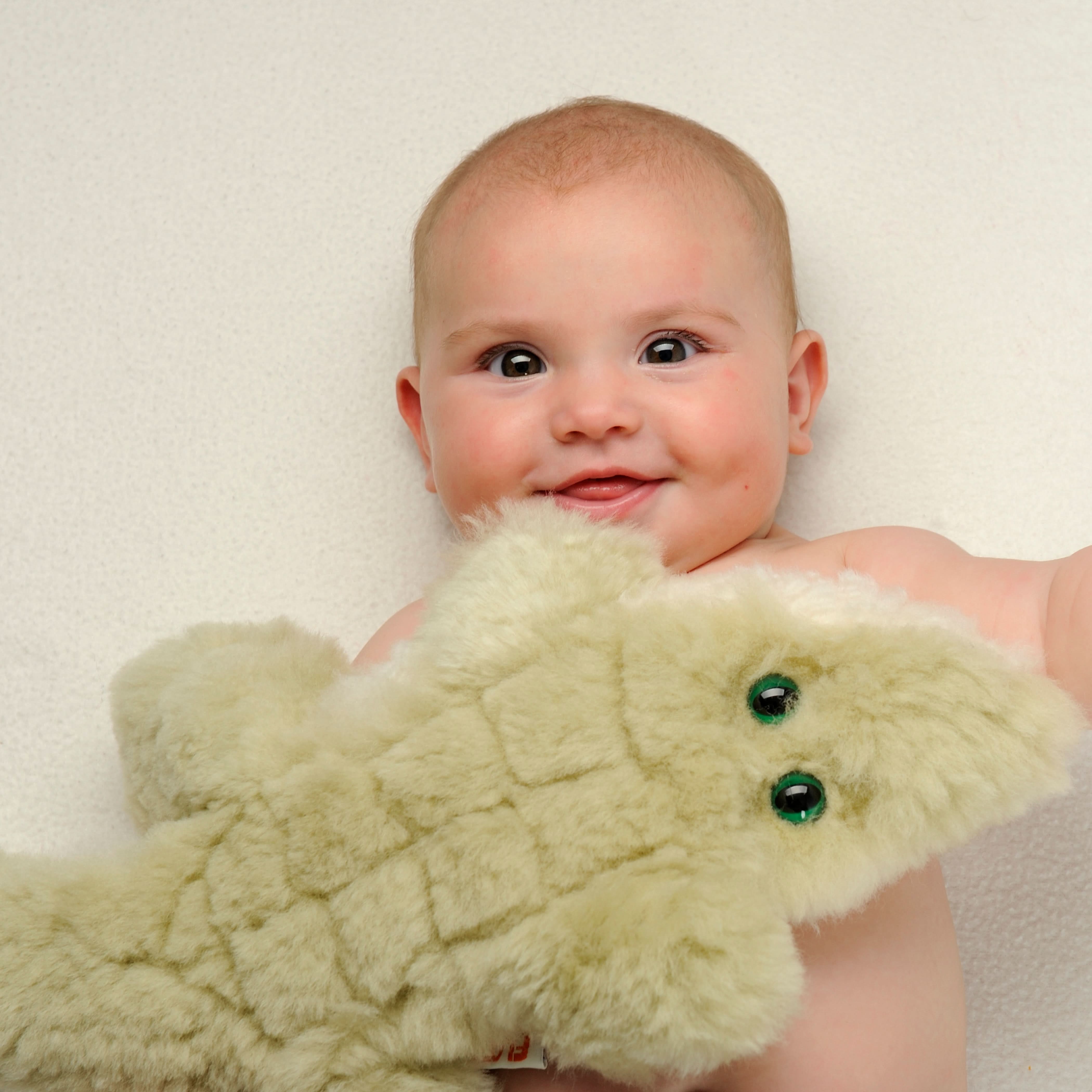 Cream sheepskin toy with green eyes held by smiling baby, front view. - Yellow Earth Australia