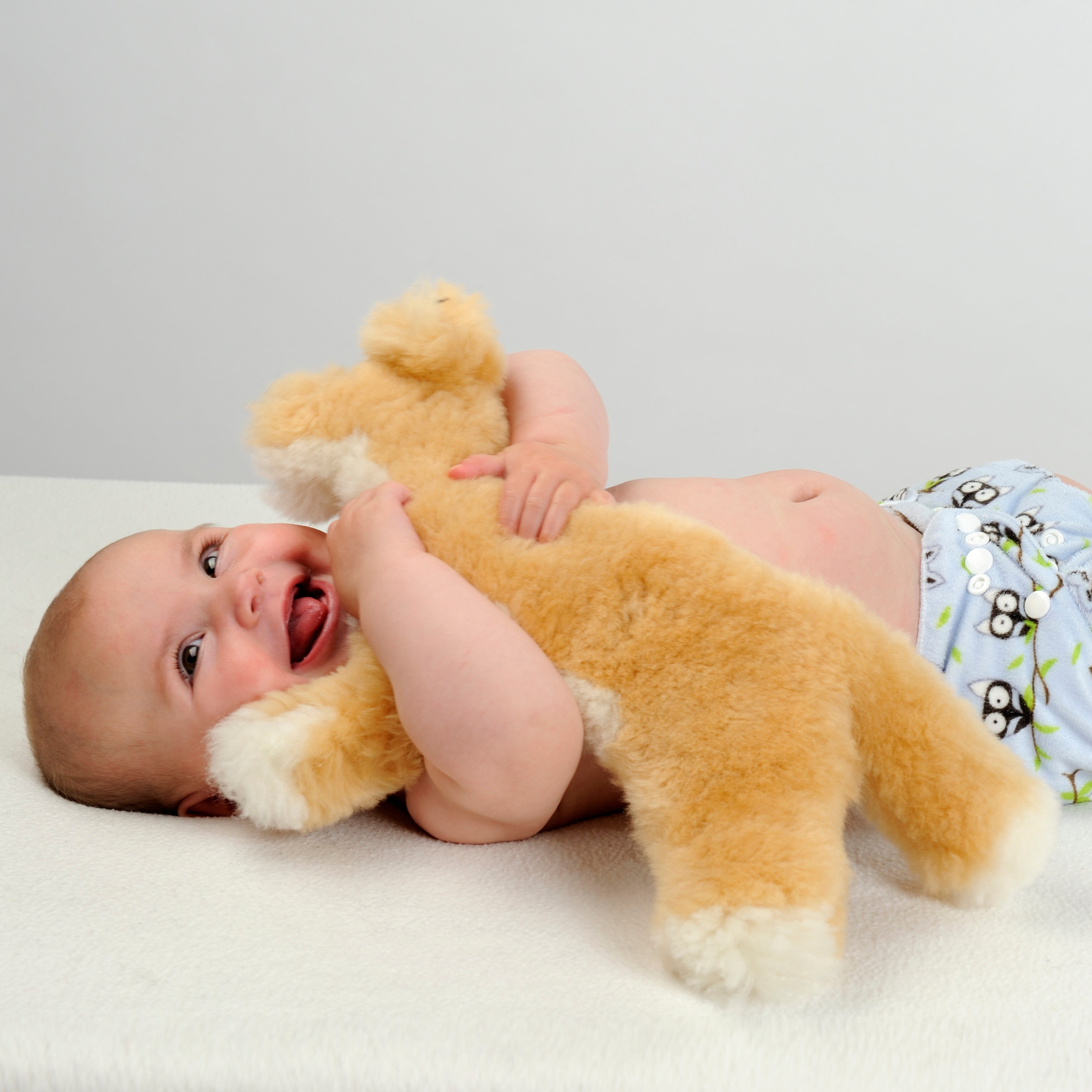 Baby hugging golden sheepskin teddy bear on white surface. - Yellow Earth Australia