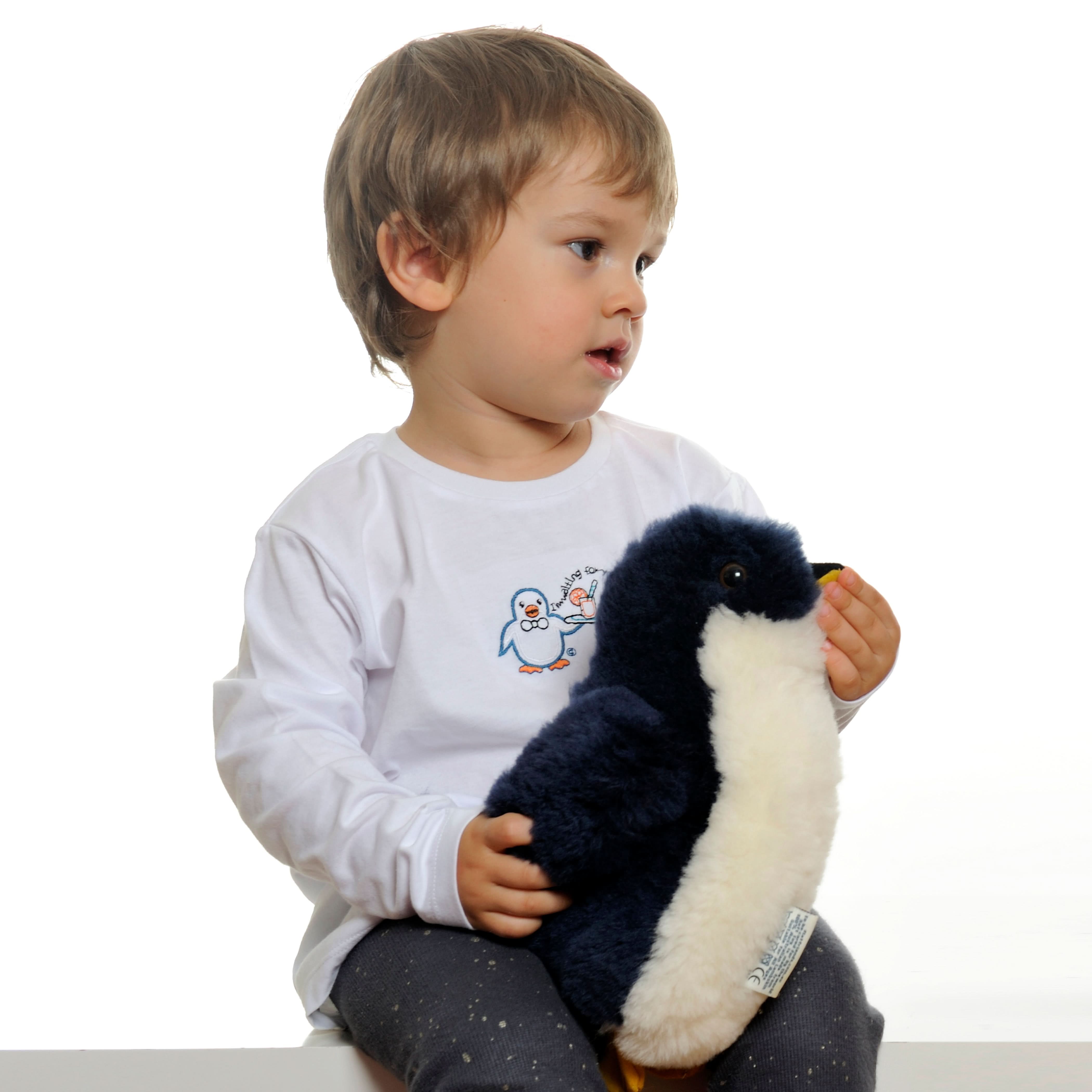 Soft black and white penguin plush toy held by toddler, side view. - Yellow Earth Australia