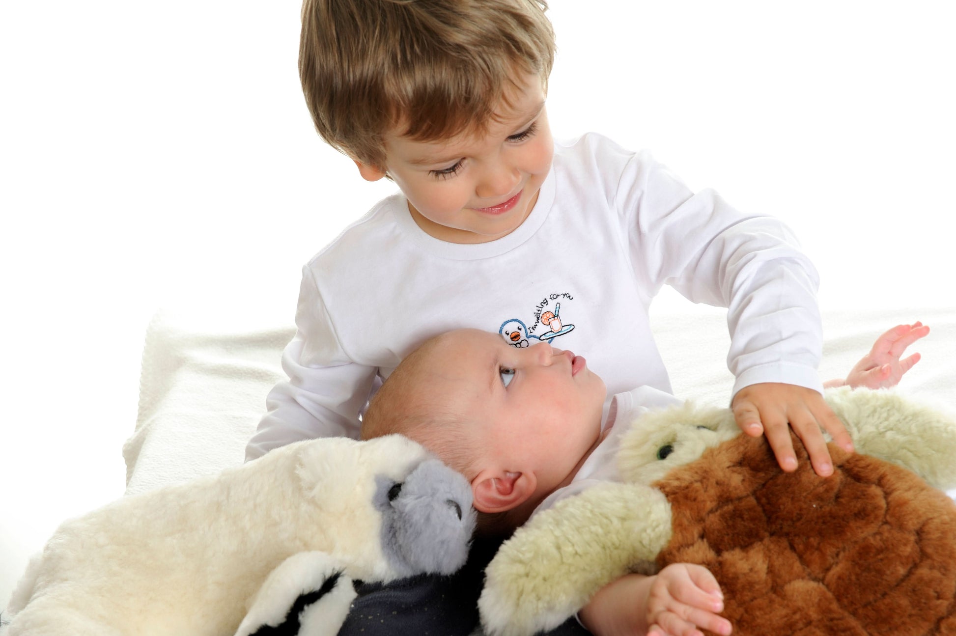 Toddler holding soft natural sheepskin and wool toys on white blanket, overhead view. - Yellow Earth Australia