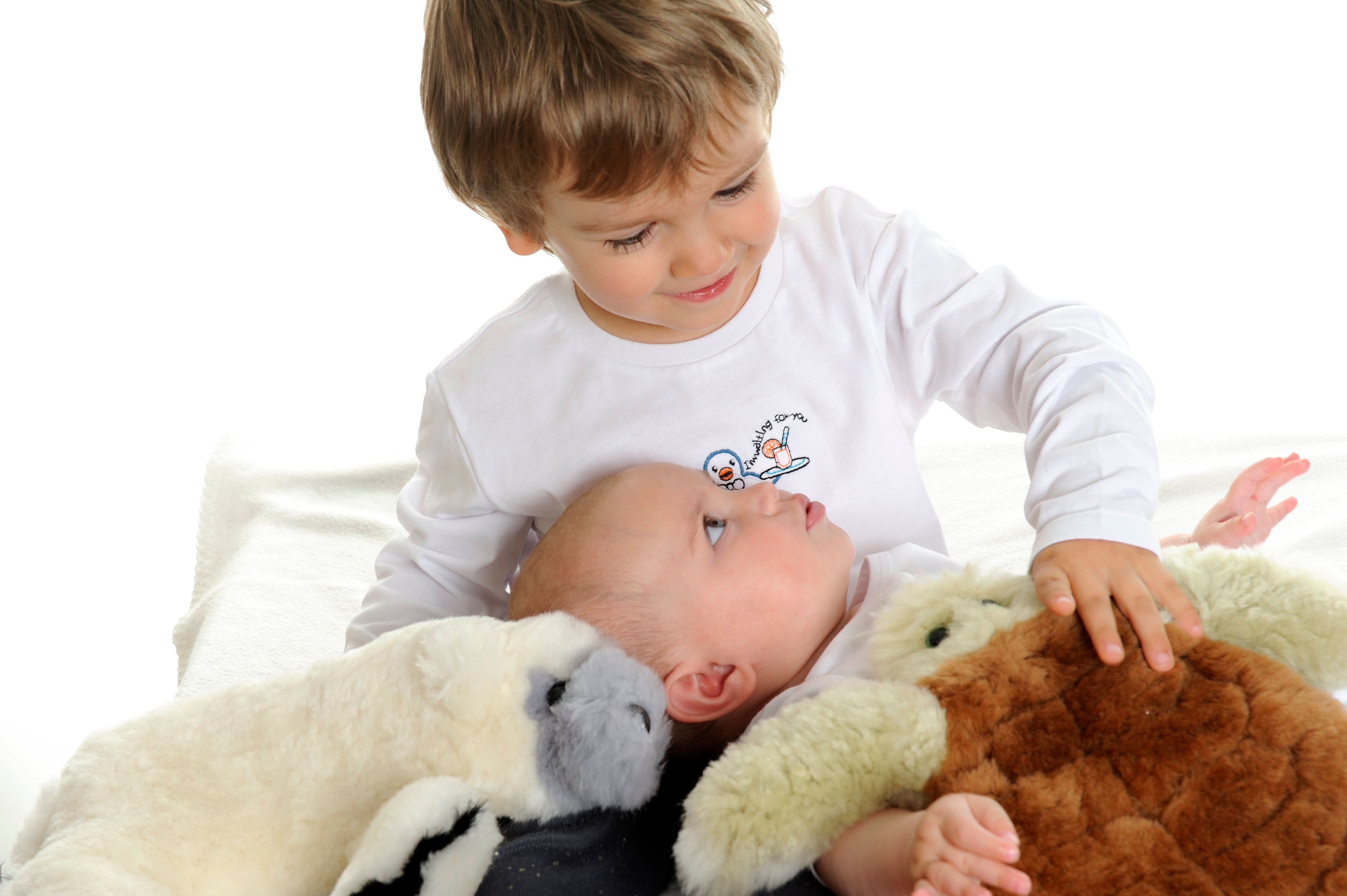 Toddler holding soft natural sheepskin and wool toys on white blanket, overhead view. - Yellow Earth Australia