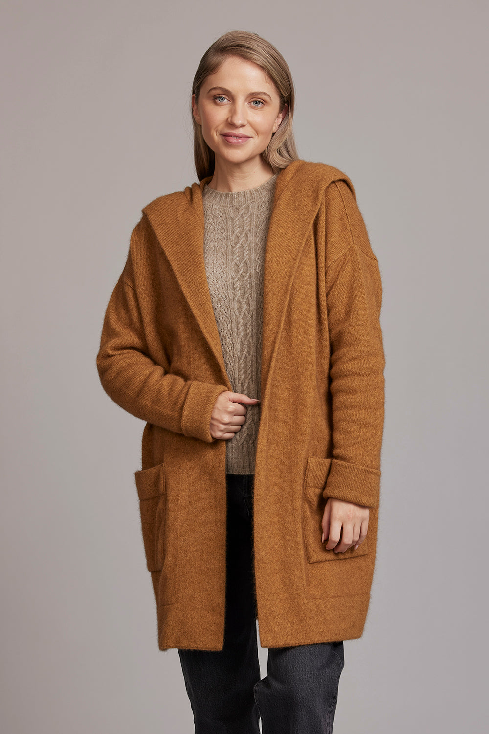 Woman wearing caramel wool cardigan over grey cable knit sweater and black pants. - Yellow Earth Australia