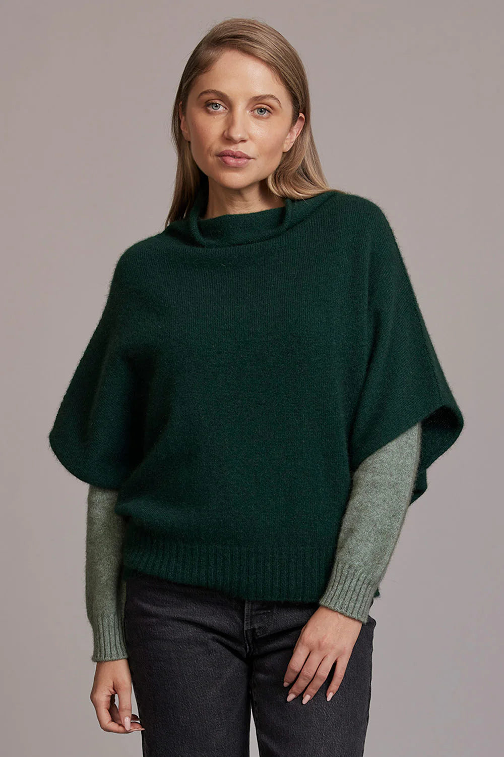 Woman wearing dark green and grey wool poncho sweater with turtleneck, front view. - Yellow Earth Australia