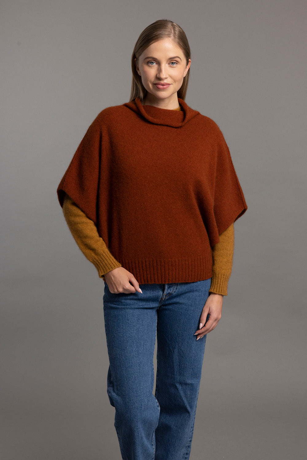 Woman wearing rust and gold colorblock wool poncho with jeans, front view. - Yellow Earth Australia