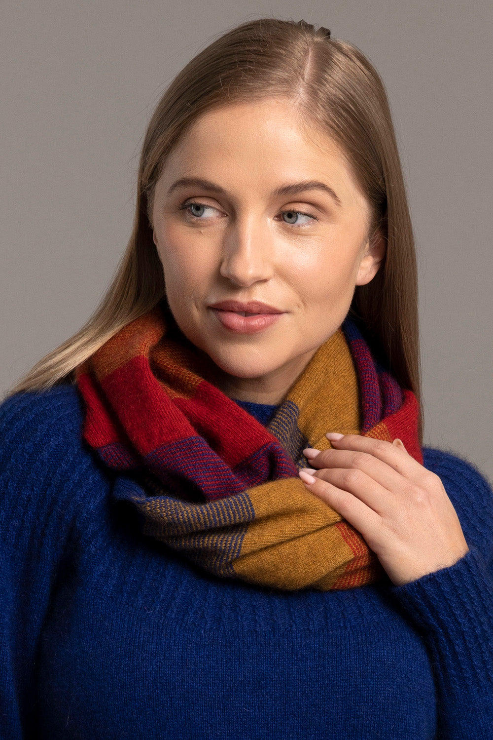 Woman wearing multicoloured striped wool scarf with blue sweater, front view. - Yellow Earth Australia