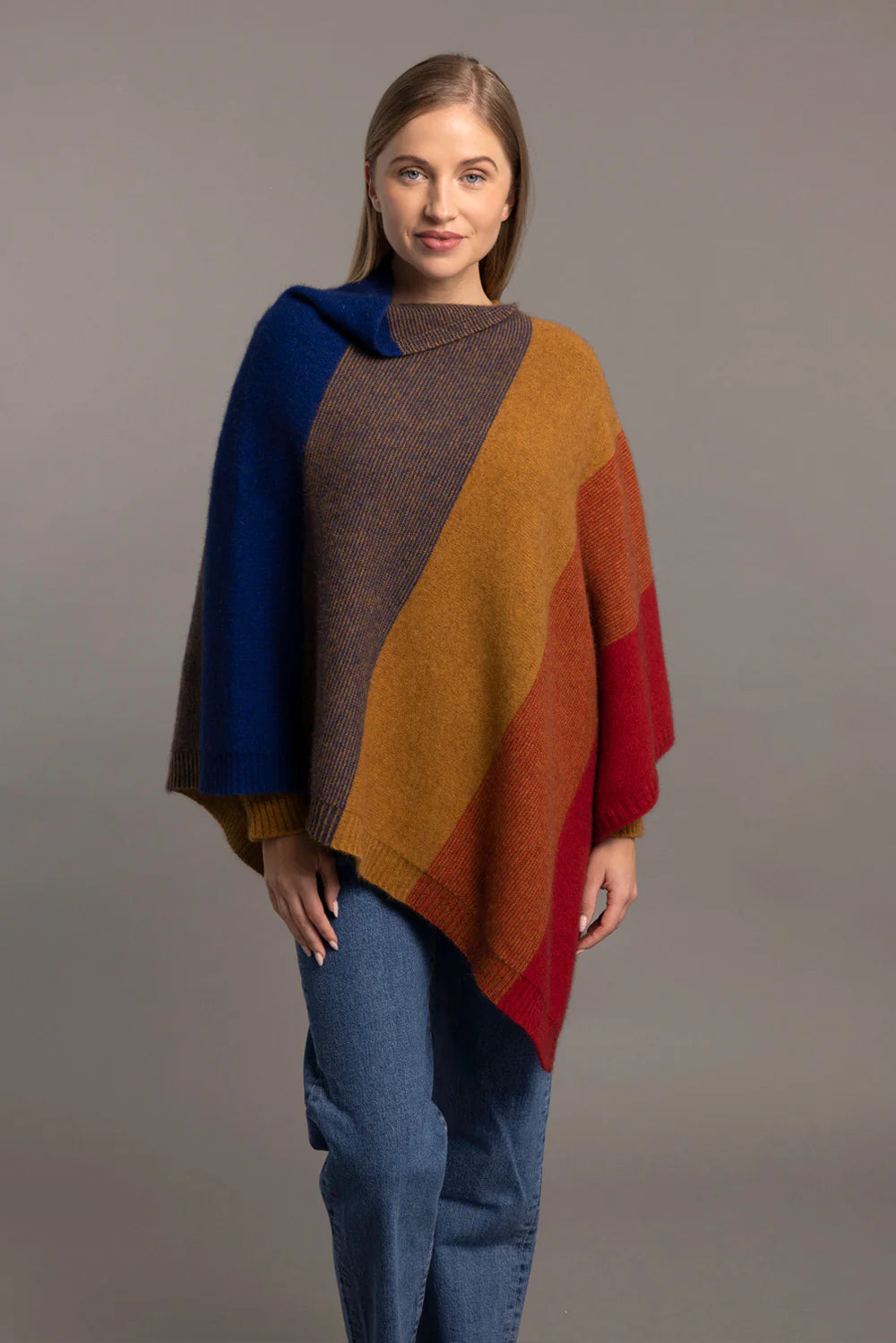 Colorblock wool poncho in blue, brown, orange and red worn with blue jeans, front view. - Yellow Earth Australia