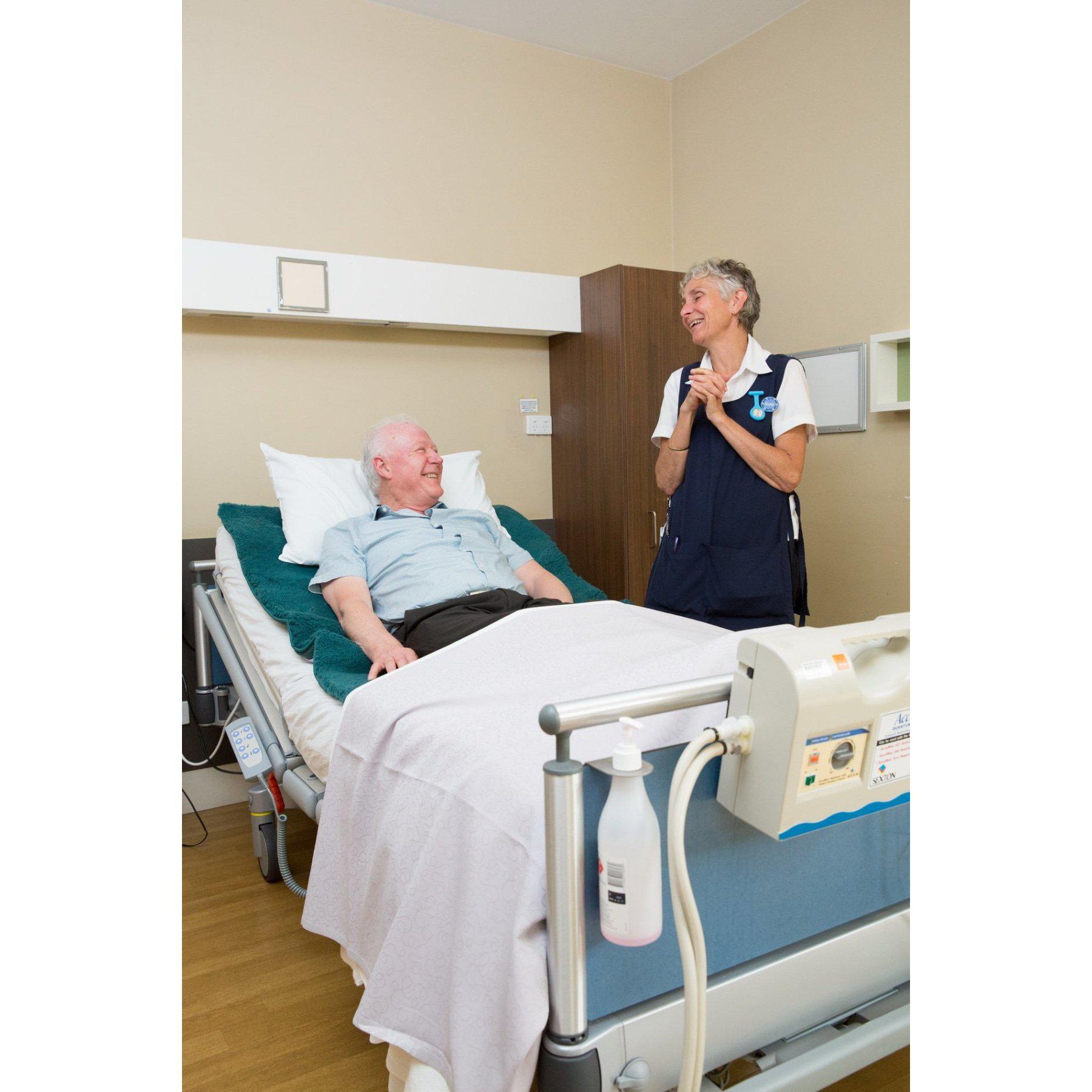Teal wool sheepskin bedcover on hospital bed with elderly patient and nurse. - Yellow Earth Australia