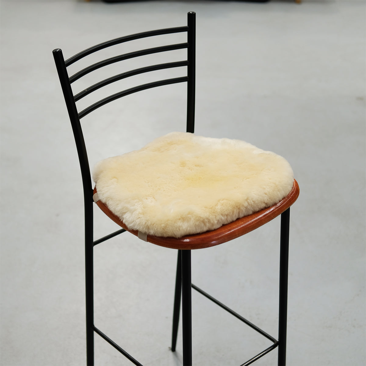 Black metal bar stool with cream sheepskin seat pad and wooden trim, front angle view. - Yellow Earth Australia