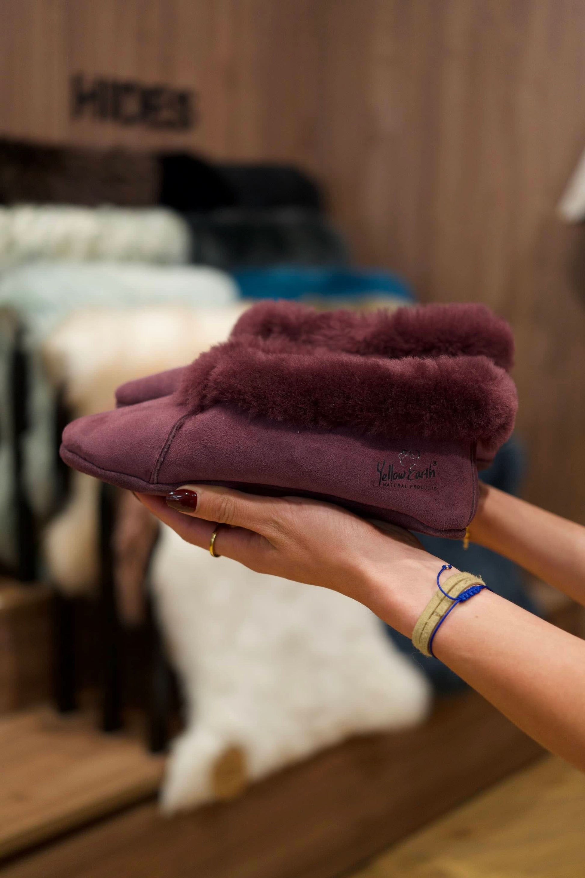 Burgundy sheepskin bootie slipper with fluffy wool collar held in hand, front view. - Yellow Earth Australia
