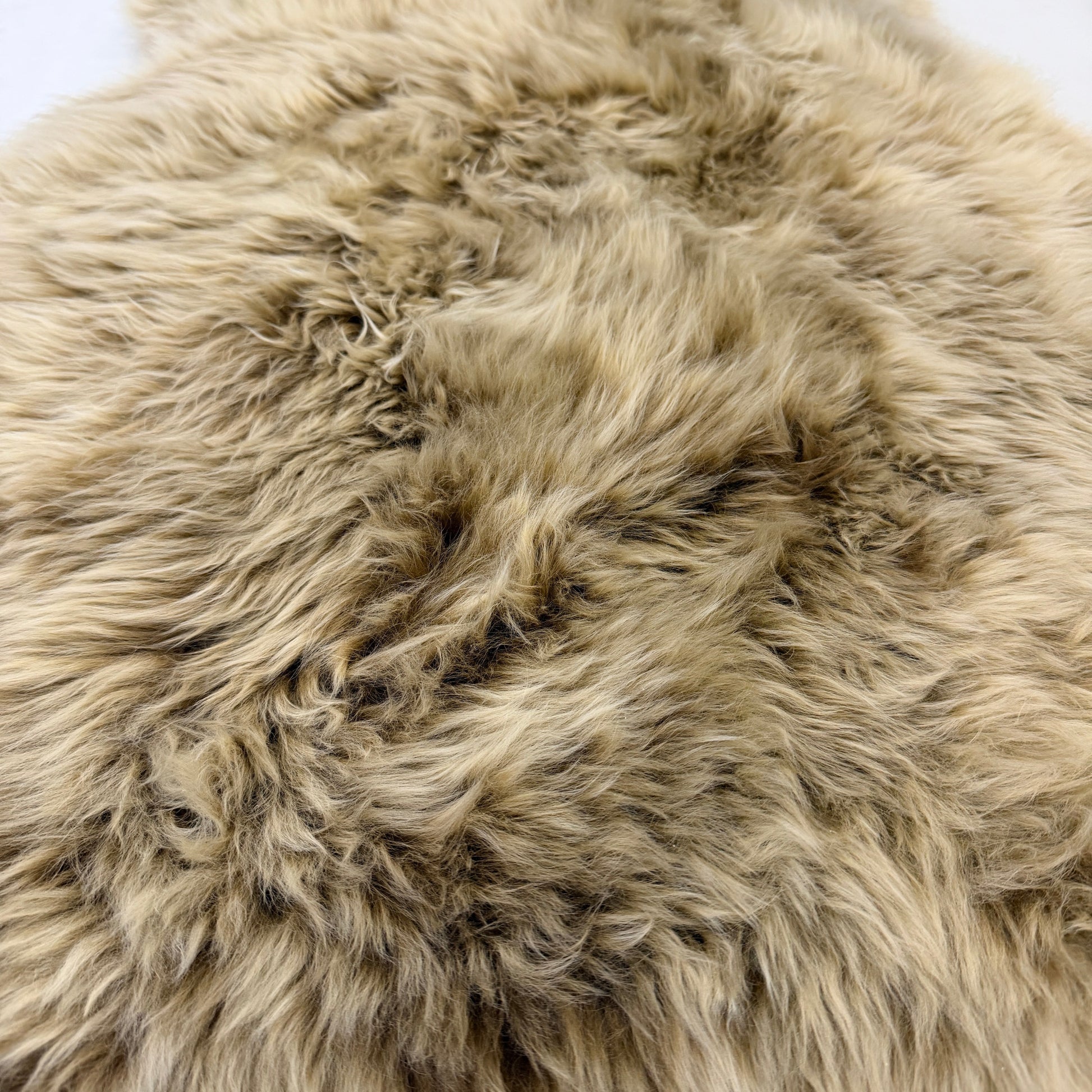 A close-up of a shaggy sheepskin rug or sheepskin-style rug in a warm taupe-beige color with natural tonal variation.