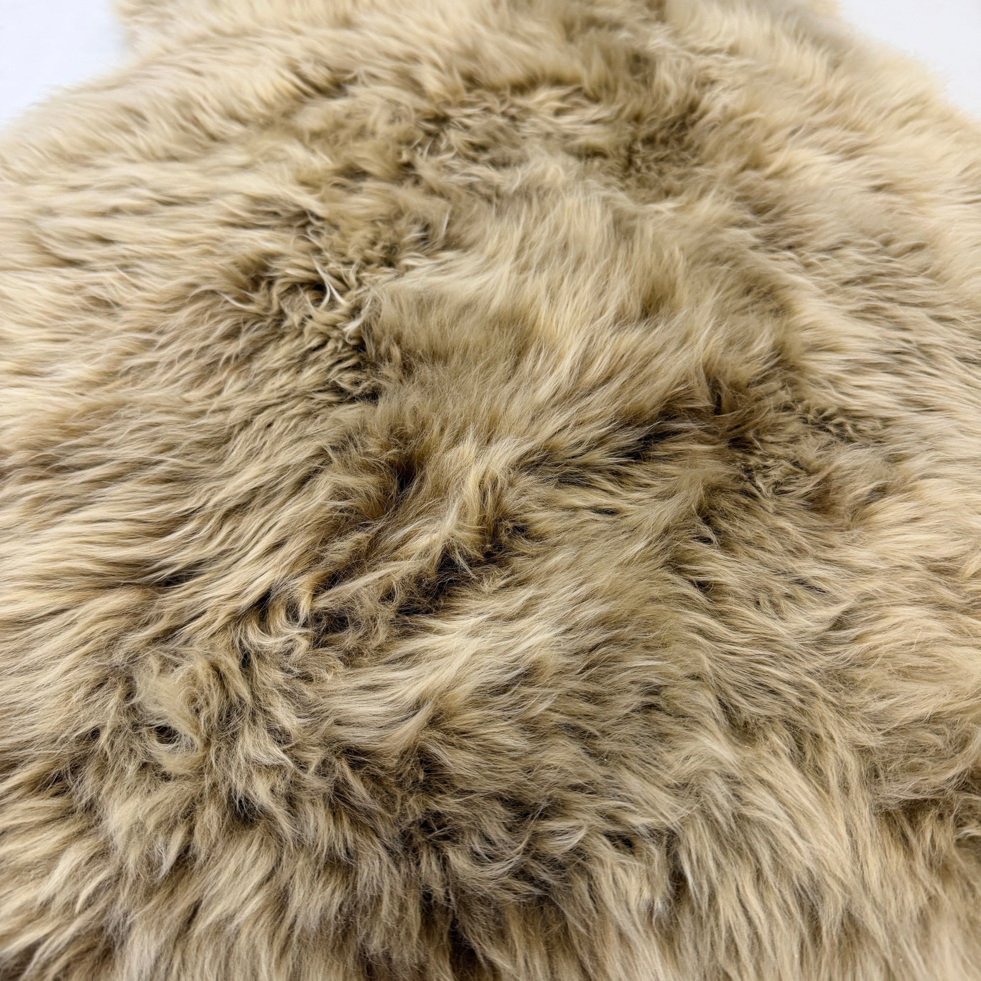 A close-up of a shaggy sheepskin rug or sheepskin-style rug in a warm taupe-beige color with natural tonal variation.