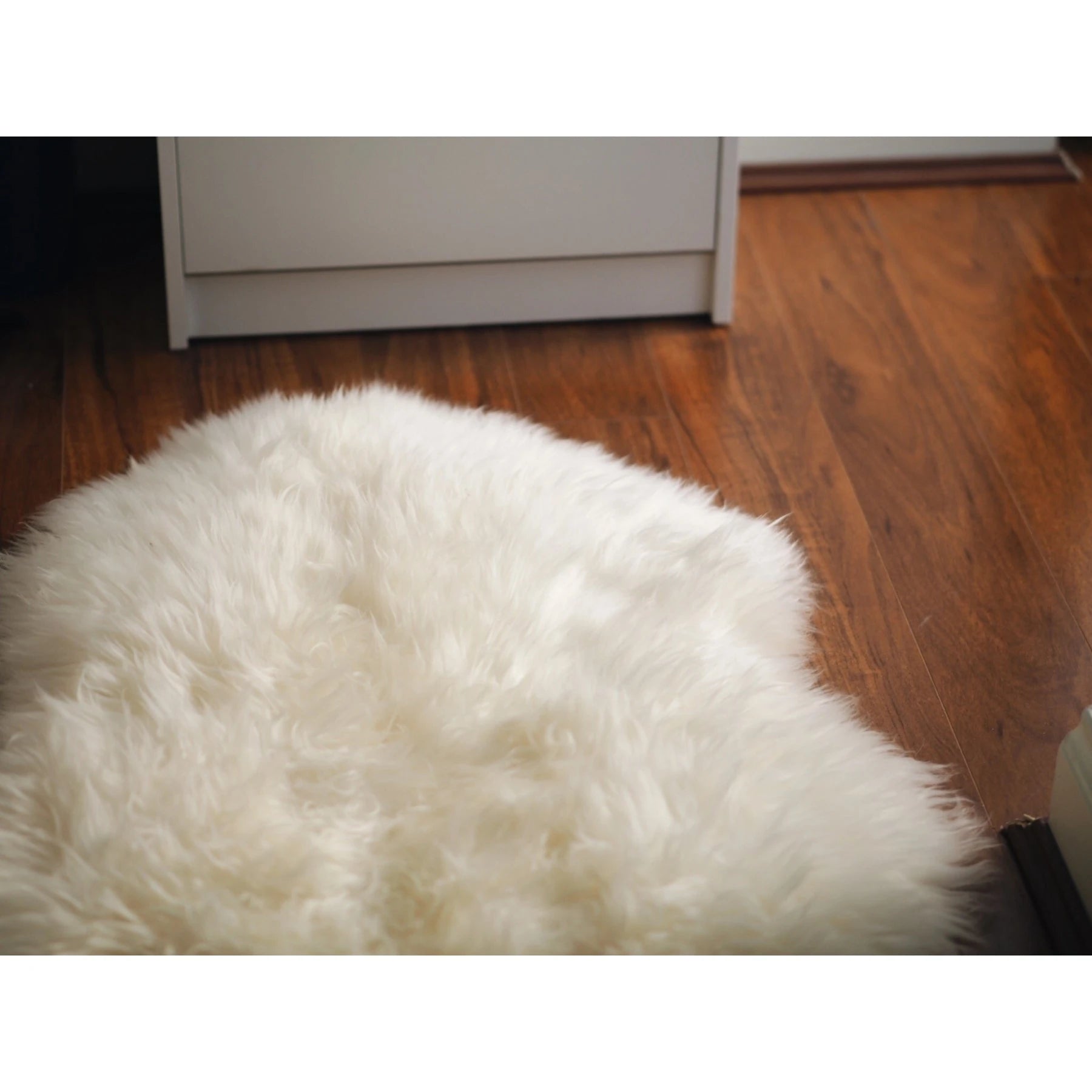 Luxurious white sheepskin rug on wooden floor, top-down view showcasing soft wool texture. - Yellow Earth Australia