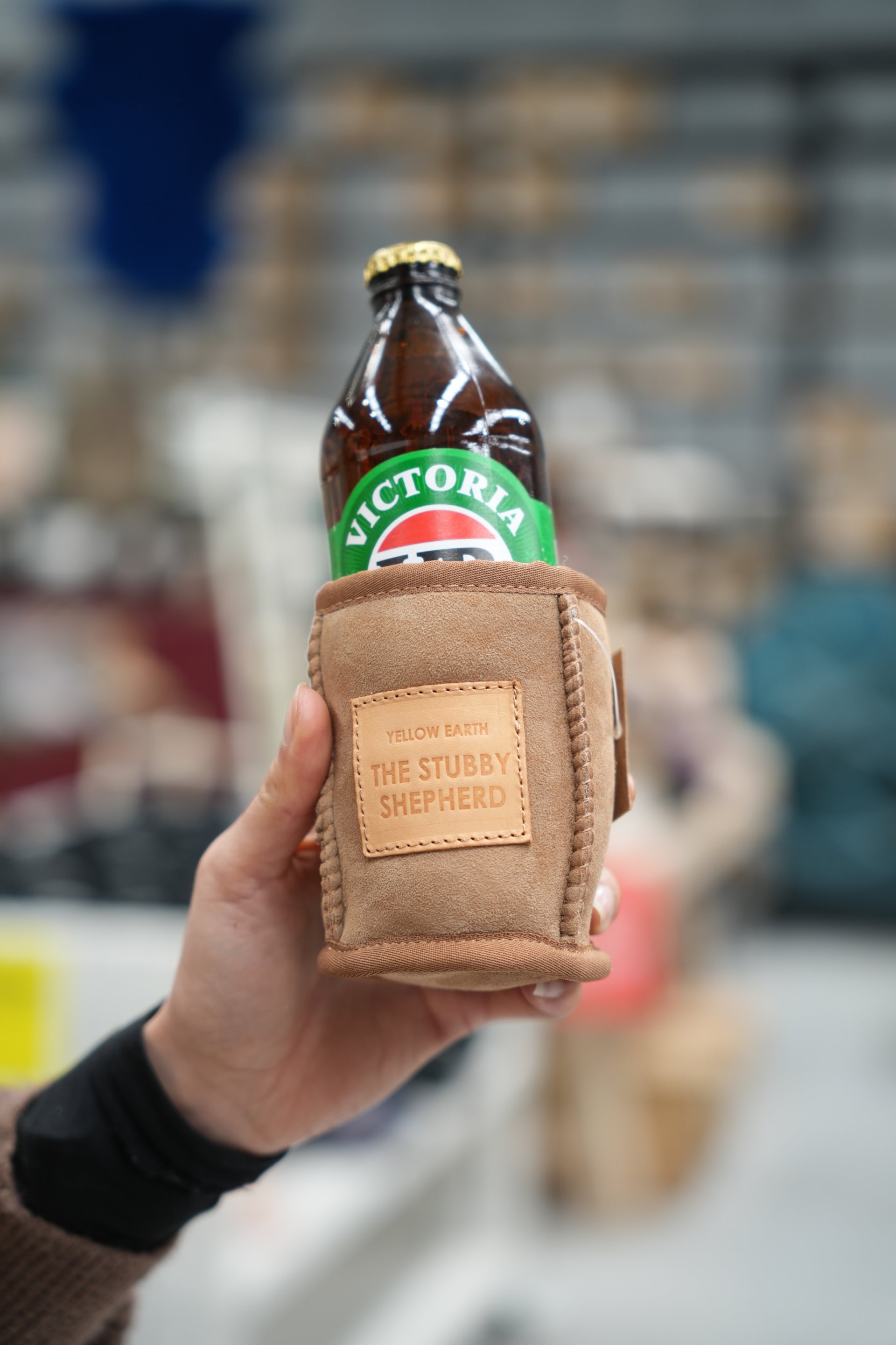 Tan suede bottle holder with leather patch, holding a beer bottle, front view. - Yellow Earth Australia