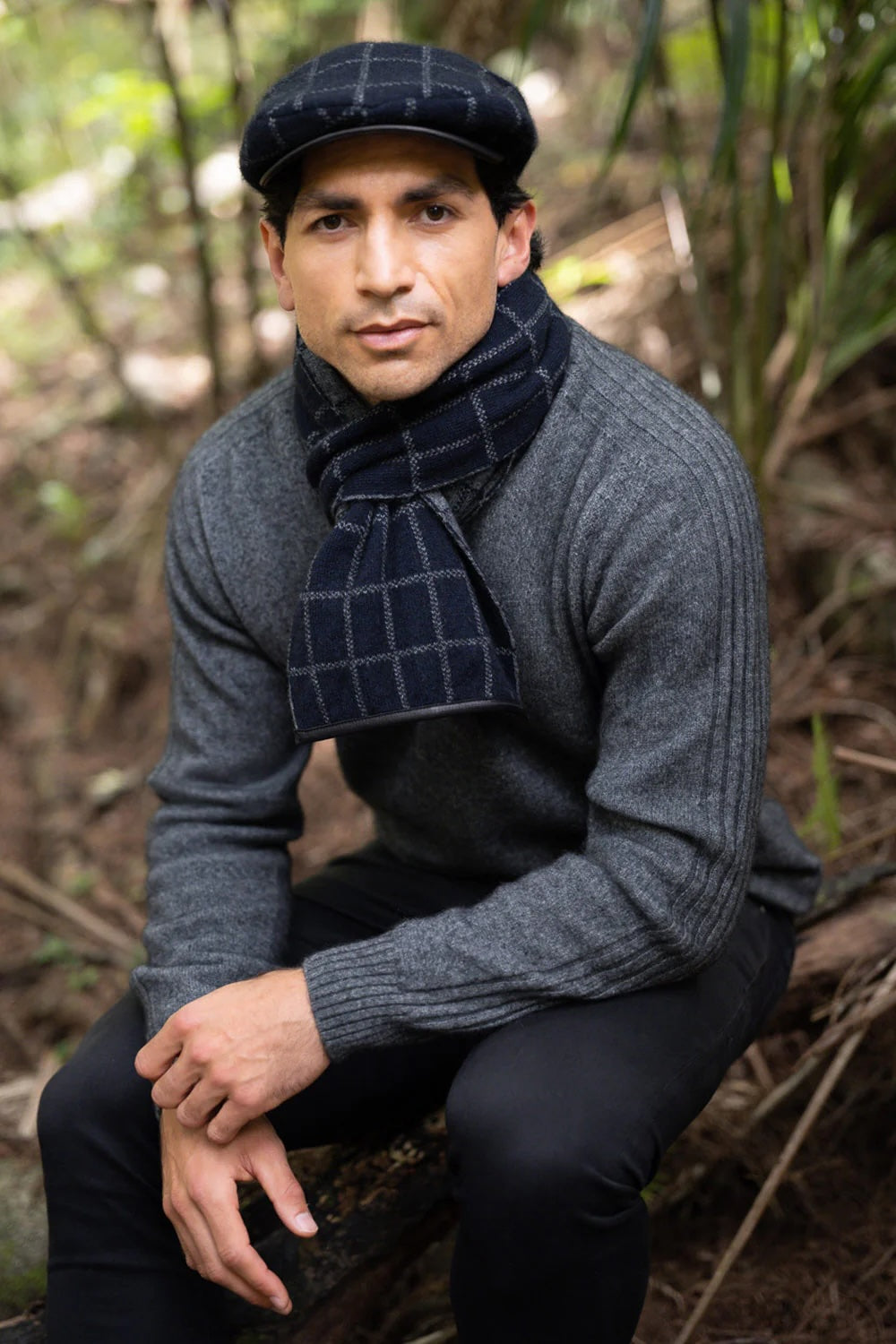 Dark charcoal wool flat cap with plaid pattern, paired with navy scarf, outdoor forest setting. - Yellow Earth Australia