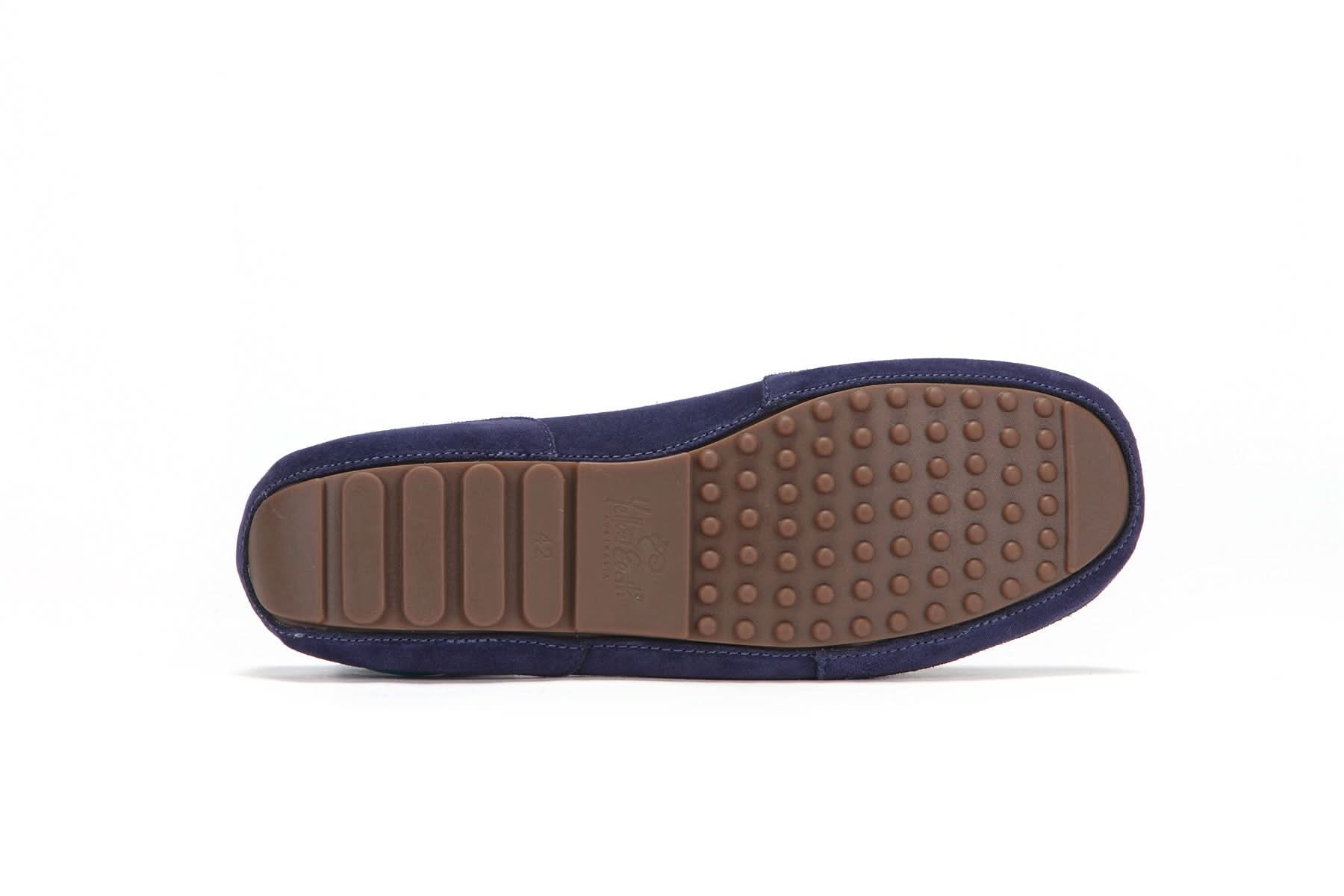 Navy suede moccasin slipper with brown rubber grip sole, shown sole side up on white background