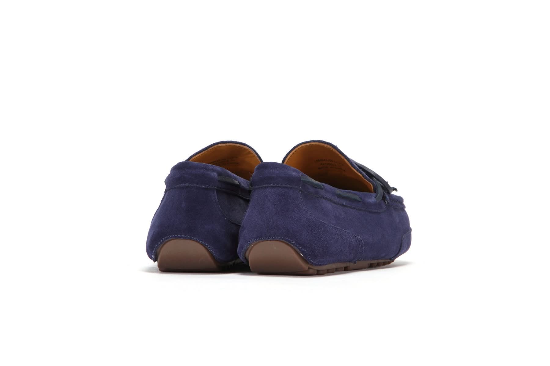 Rear view of navy blue suede moccasin shoes with brown rubber soles on white background