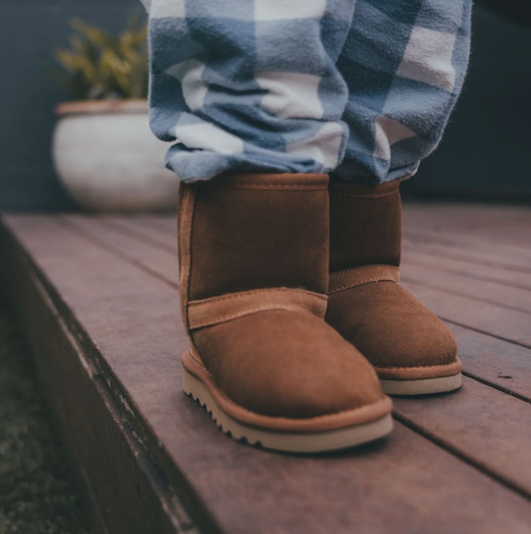 Chestnut sheepskin boots with checkered socks on wooden deck, front view. - Yellow Earth Australia