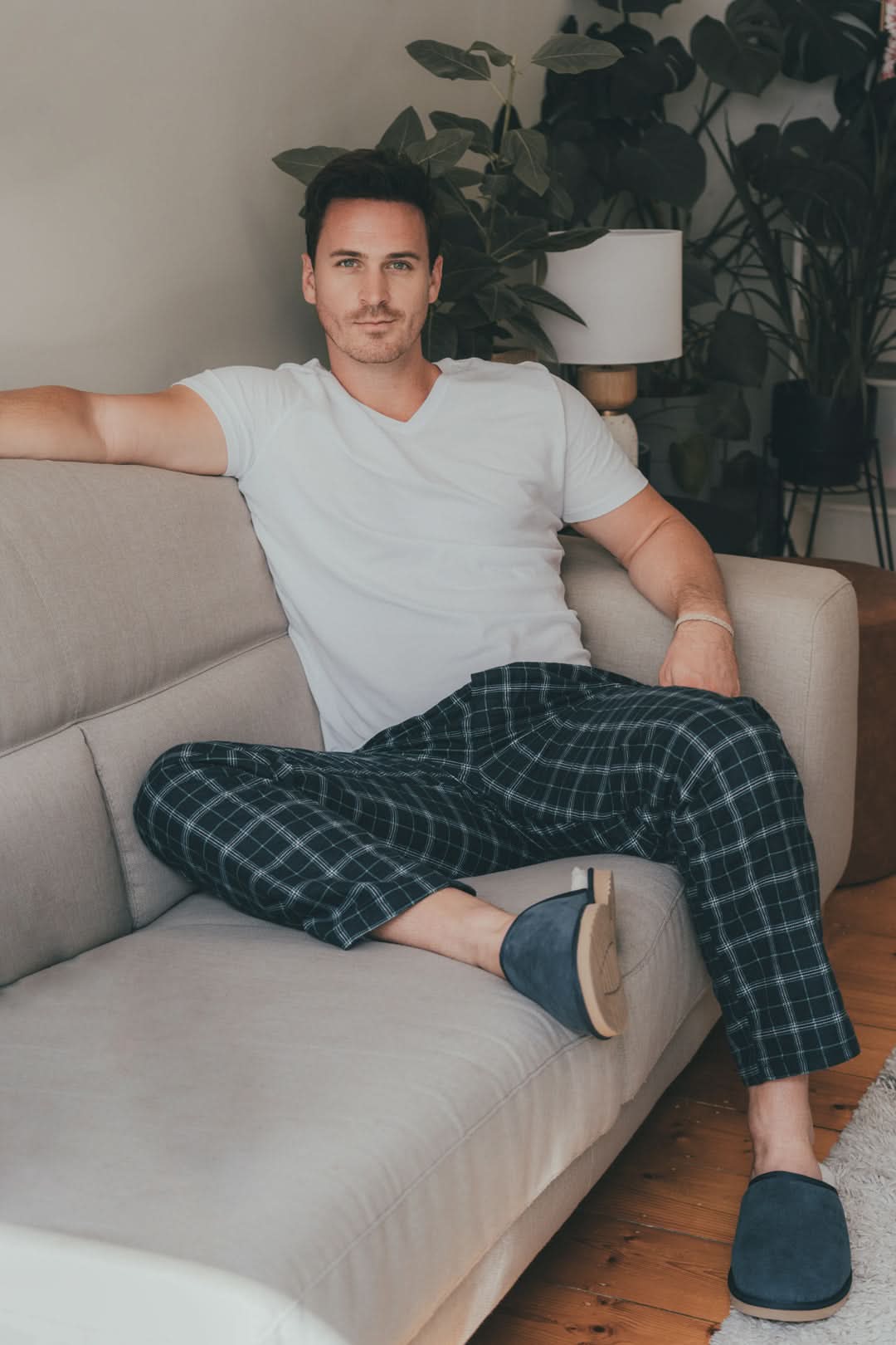 Navy plaid wool pajama pants on male model seated on beige couch. - Yellow Earth Australia