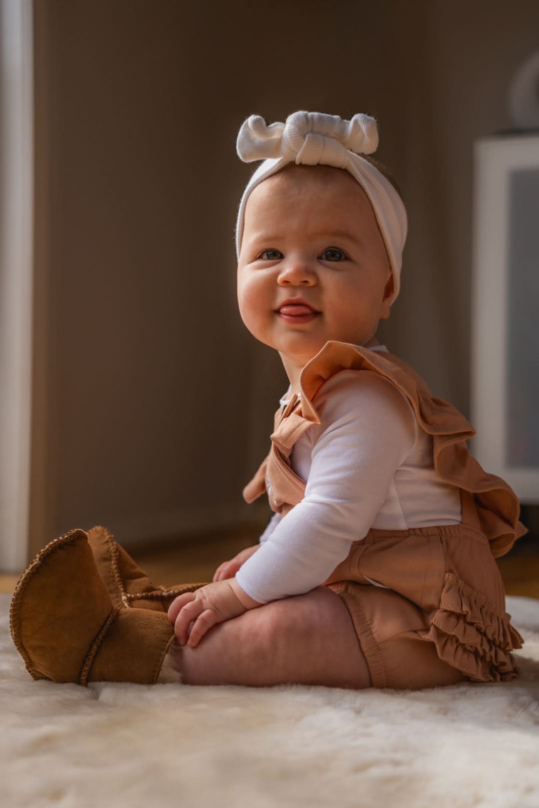 Baby sheepskin booties in tan with white headband sitting on cream wool rug. - Yellow Earth Australia