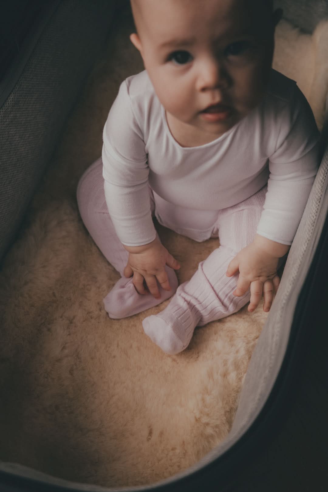 Baby wearing pink merino wool long-sleeved top and socks on natural sheepskin, overhead view. - Yellow Earth Australia