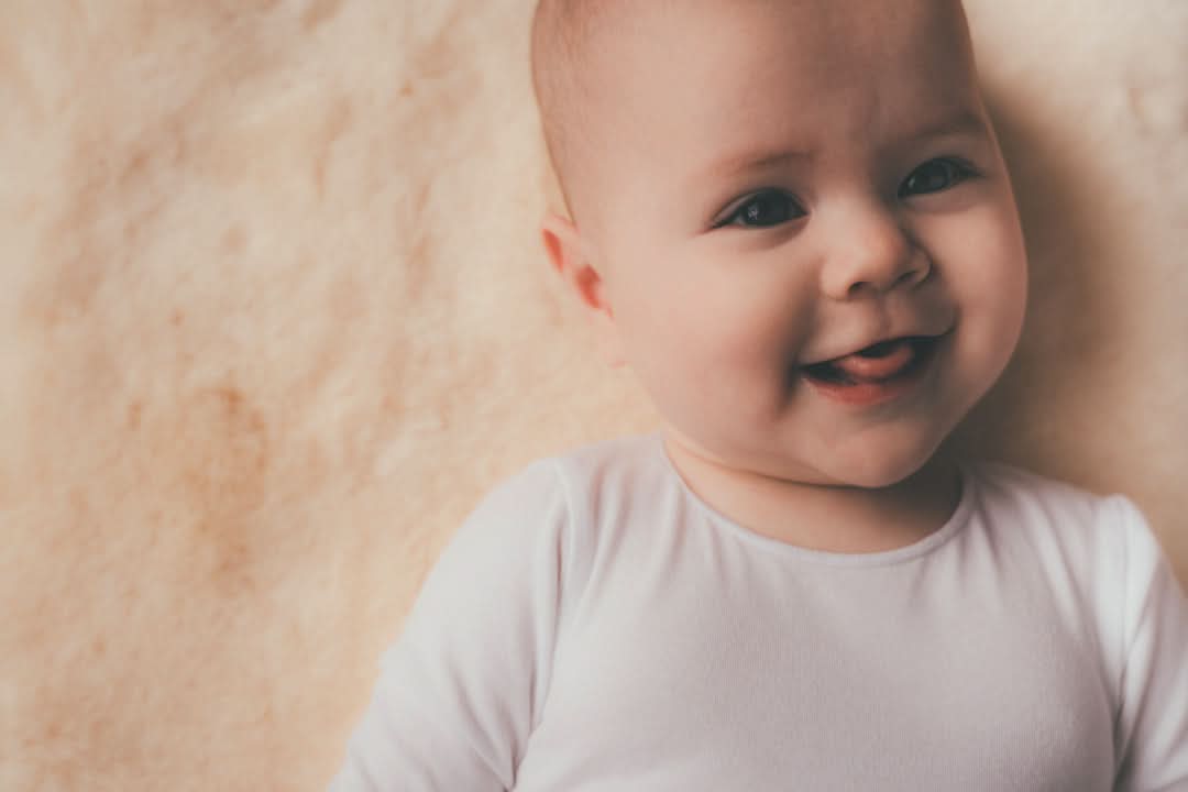 Happy baby wearing soft white merino wool bodysuit against neutral background. - Yellow Earth Australia