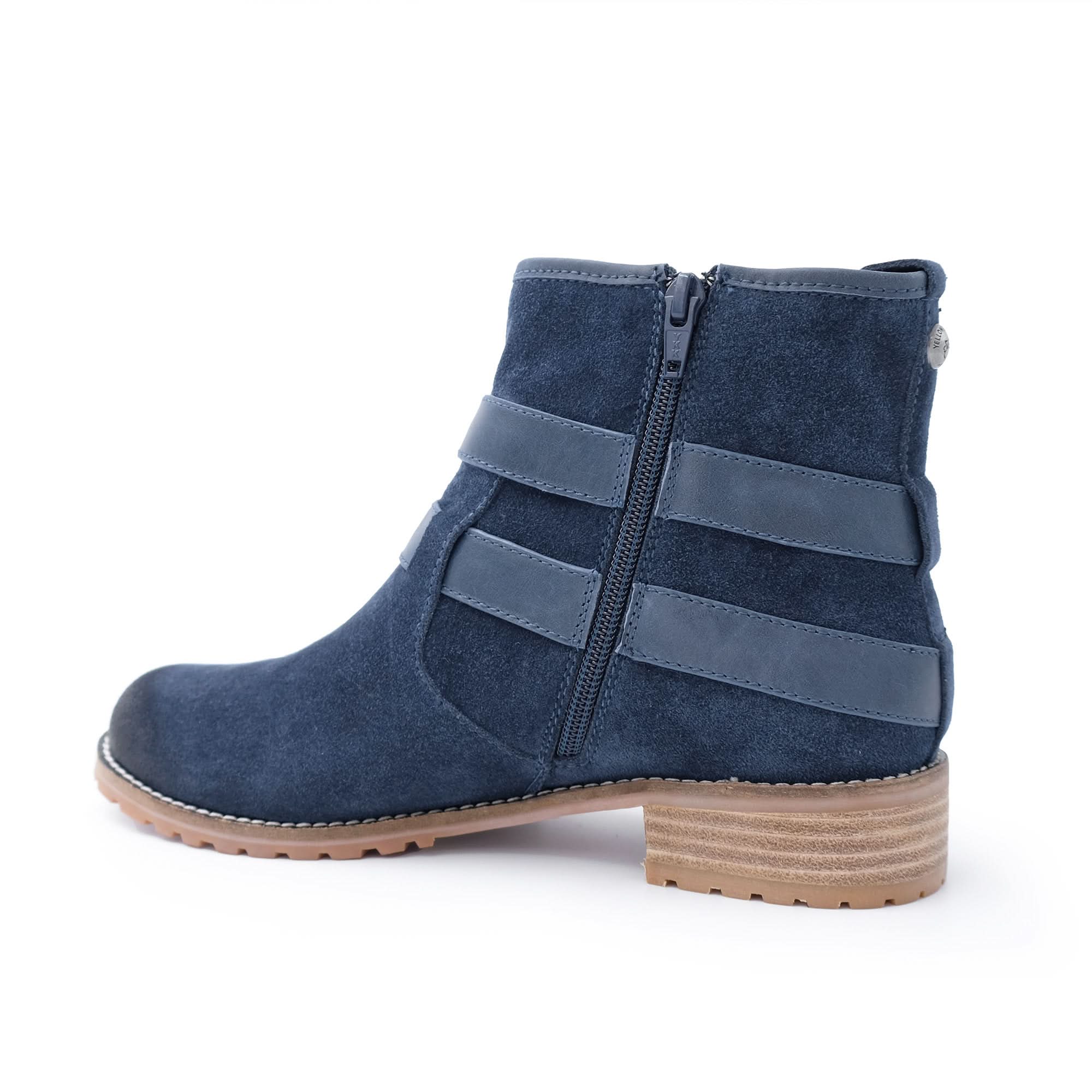 Navy blue suede ankle boot with side zipper, leather straps, and low wooden heel on white background