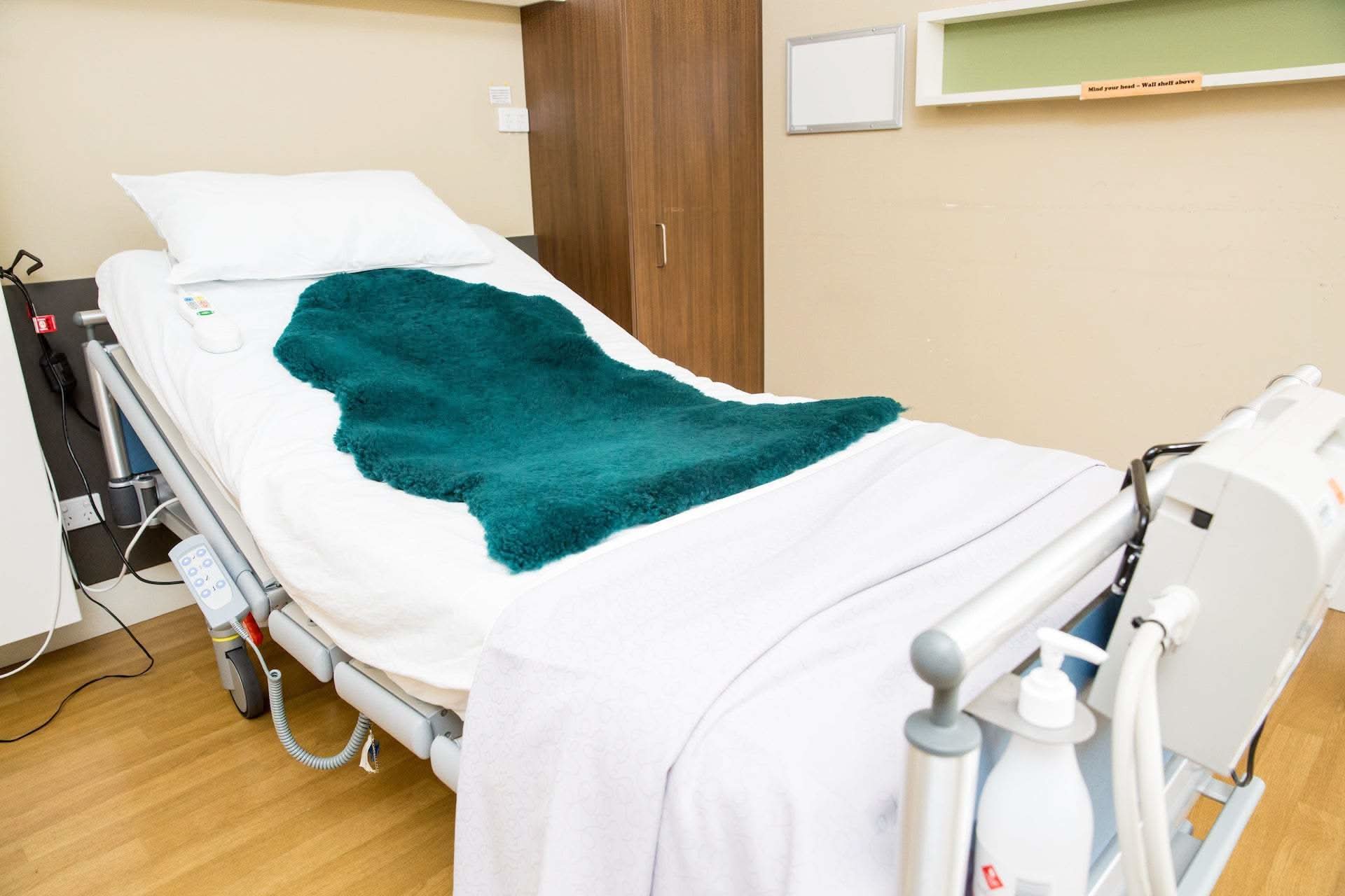 Teal sheepskin rug on white hospital bed with medical equipment visible. - Yellow Earth Australia